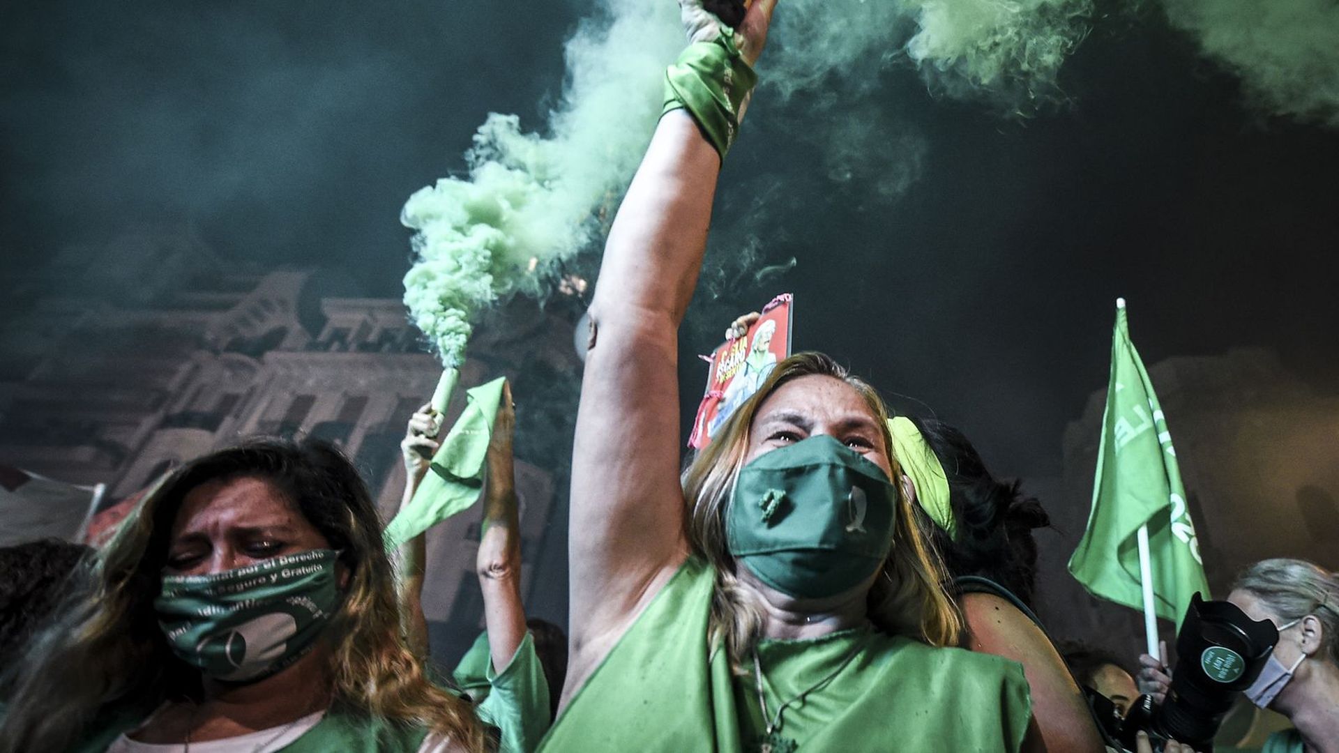 women dressed in all green clothing and wearing green masks celebrate the legalization of abortion in Argentina, waving sticks that emit green smoke in the air