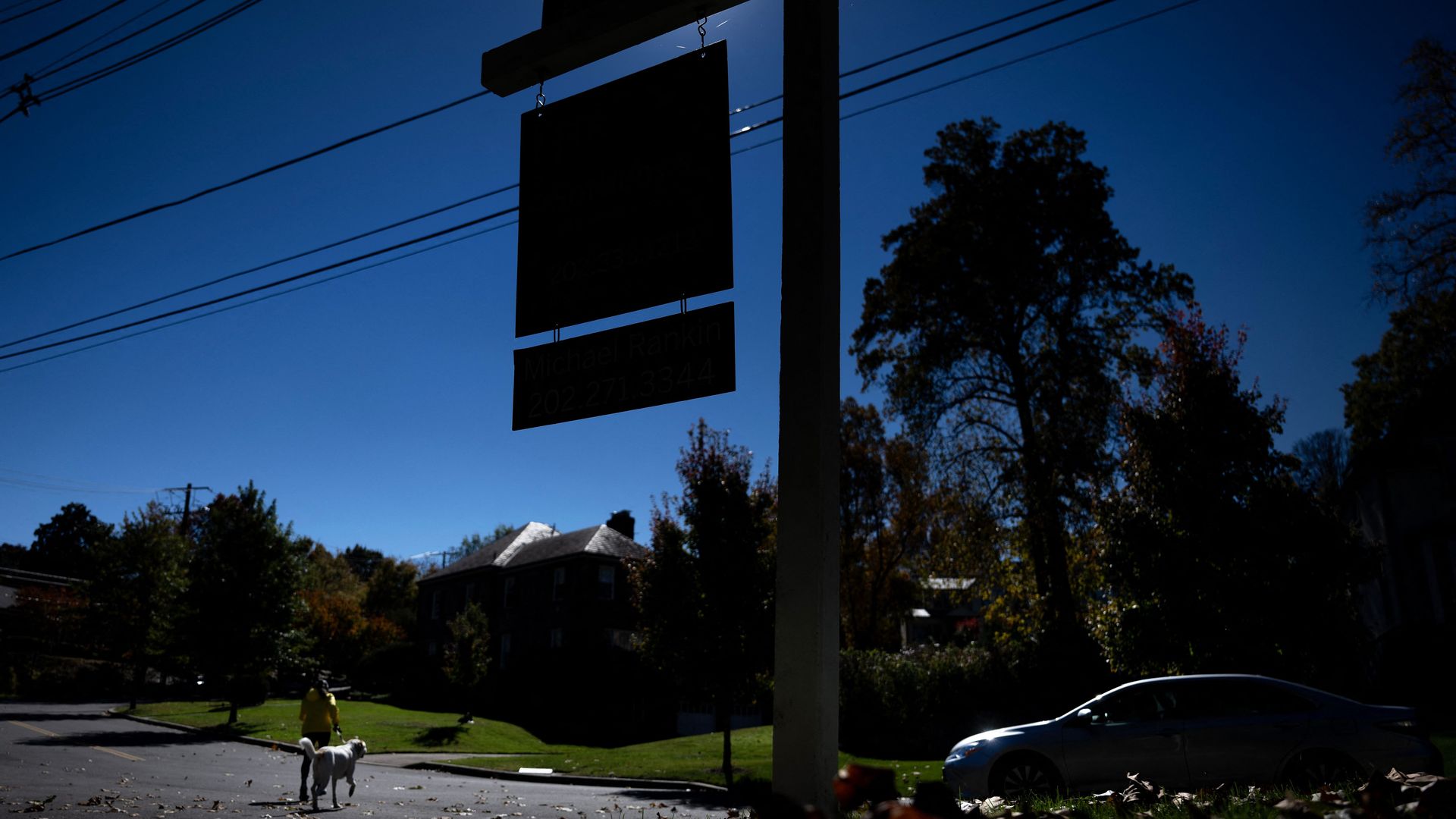 A home for sale sign darkened by shadows.