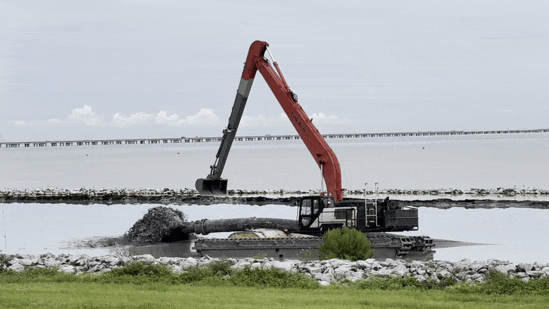 Image shows heavy equipment in the water with a pipe with mud.