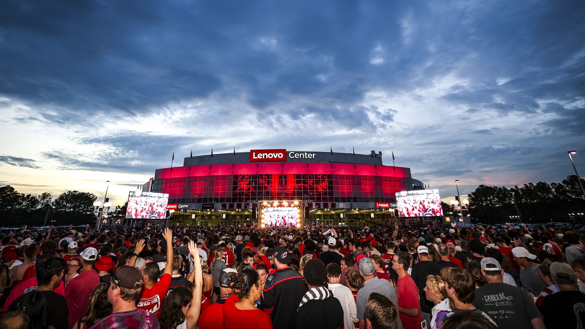 Fans cheer at the Hurricanes Watch Party for Game Six of the 2026 Stanley Cup Final outside Lenovo Center at dusk.