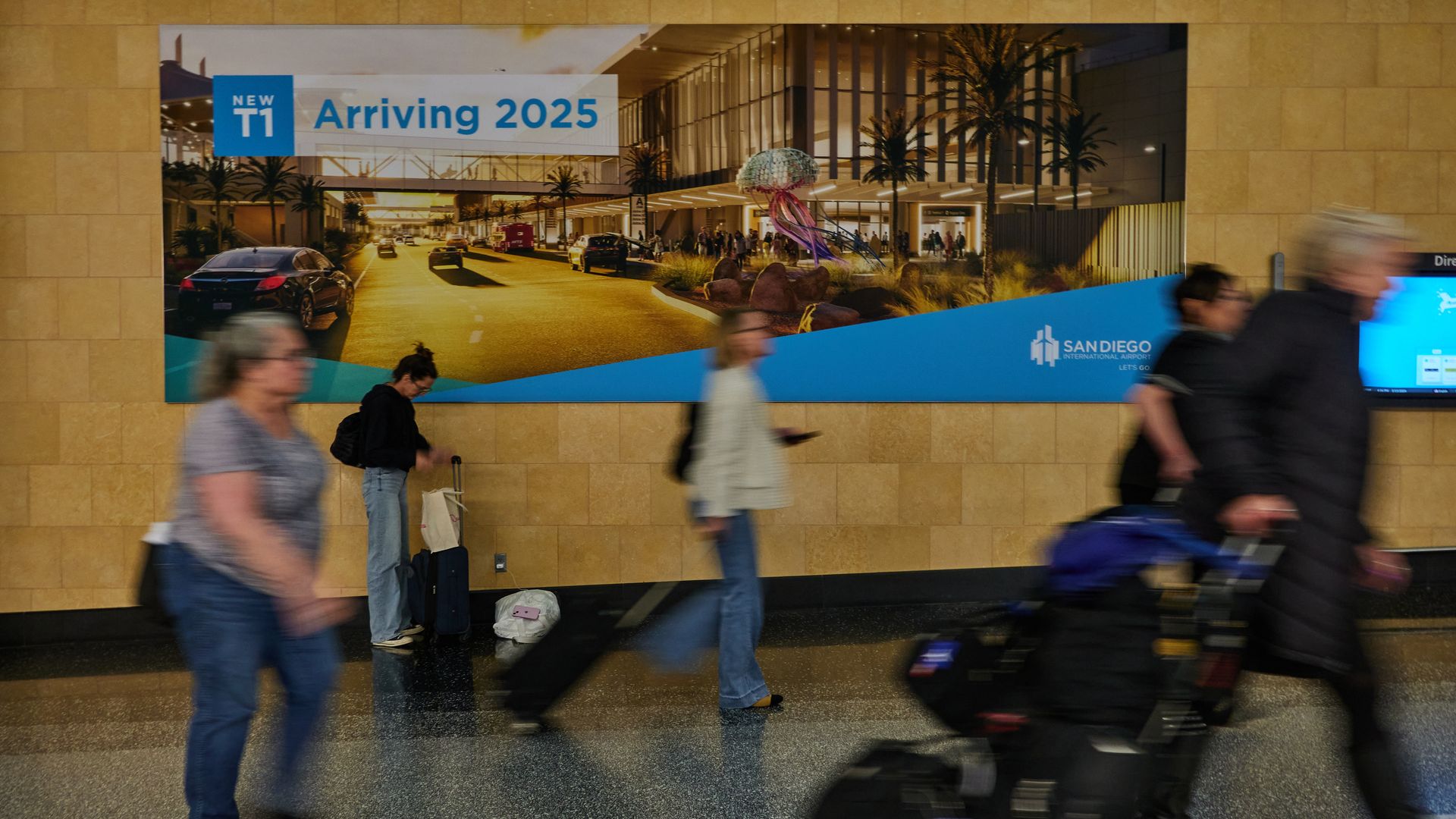 Blurred passengers walk past a sign advertising the new airport terminal