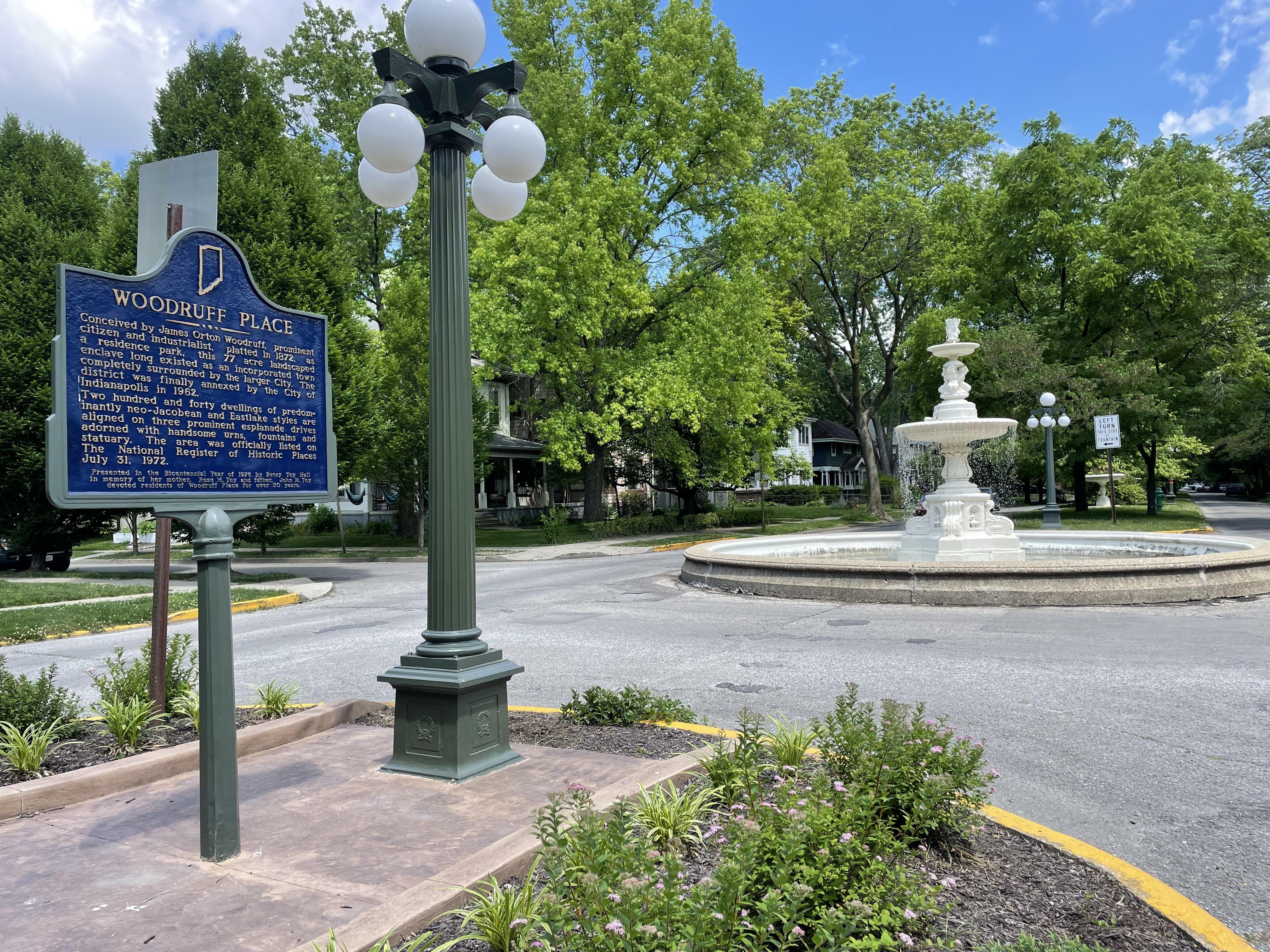 A historical marker sign to the left and a fountain to the right.