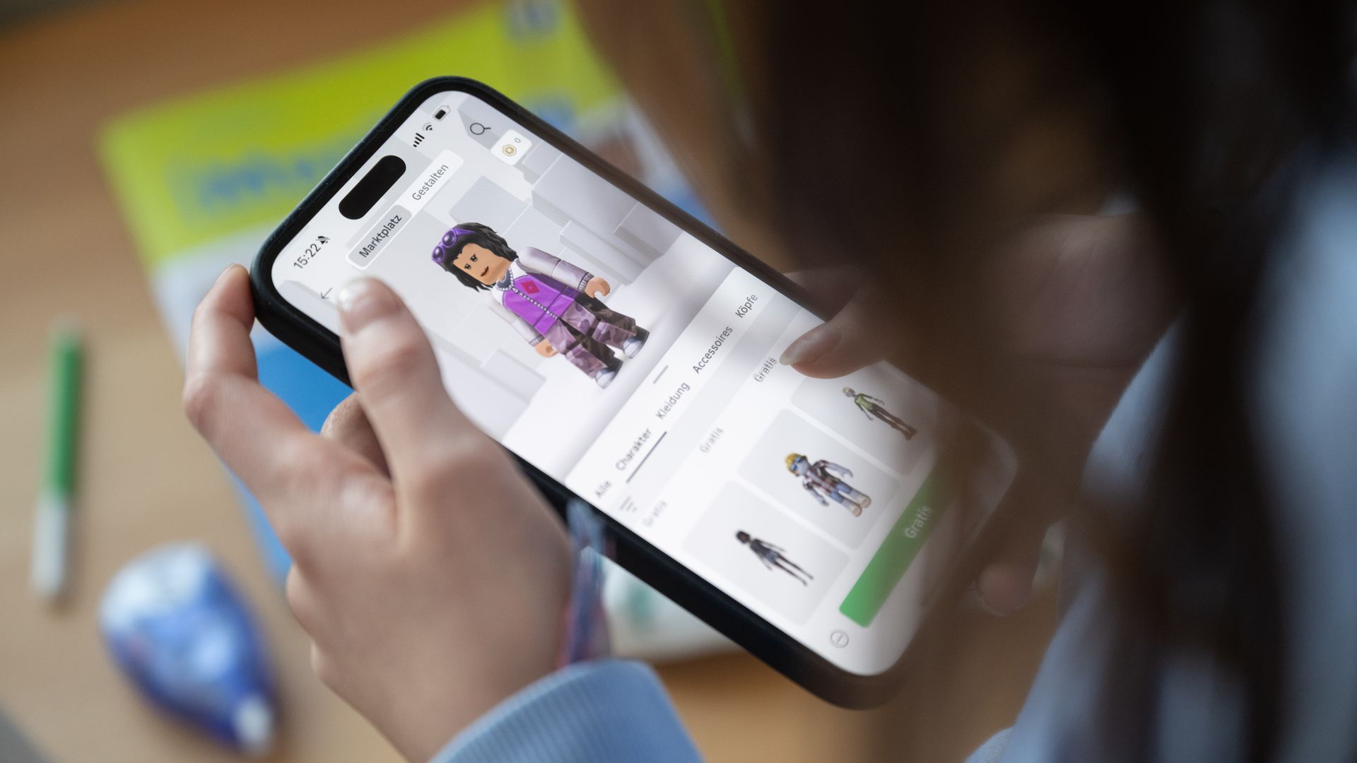 Close-up of a person holding a smartphone displaying a character customization screen with an avatar wearing purple and white clothes, browsed in a virtual marketplace app.