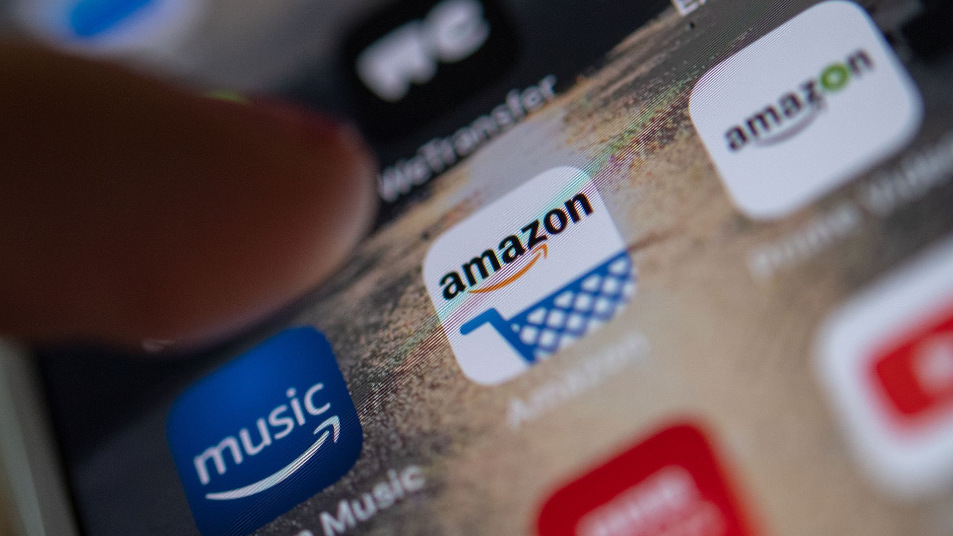 In this image, an index finger reaches to tap an Amazon app on a smart phone.