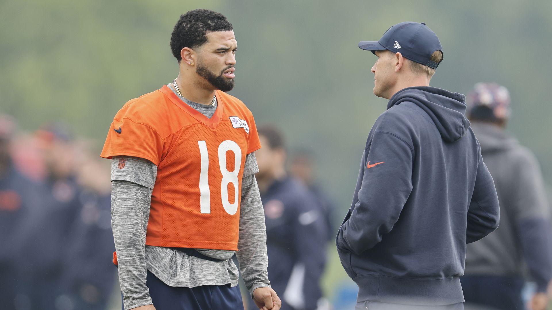 Photo of a player in a uniform talking to a coach on a practice field 