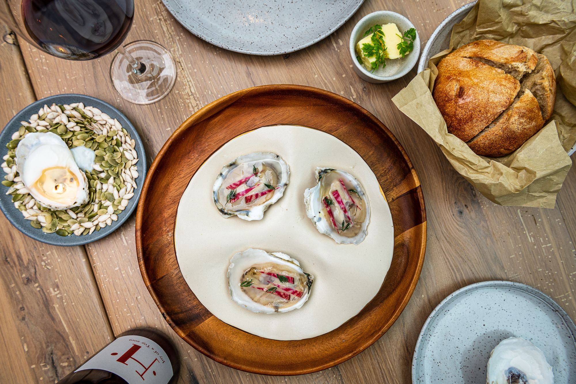 Oysters on a white plate over a wood plate next to an oyster candle, loaf of bread