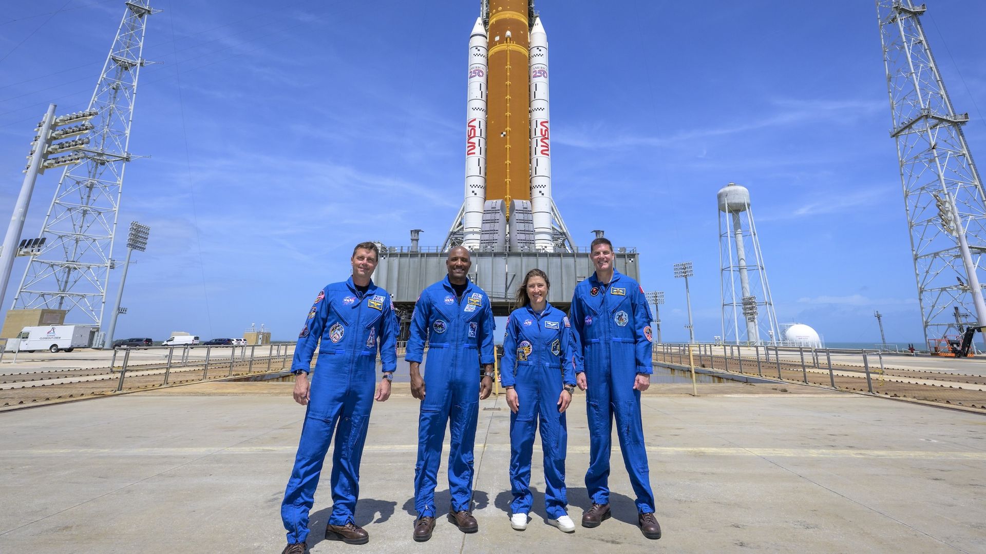 NASA astronauts Reid Wiseman, Victor Glover, Christina Koch and Jeremy Hansen in blue space suits in front of the Orion spacecraft.