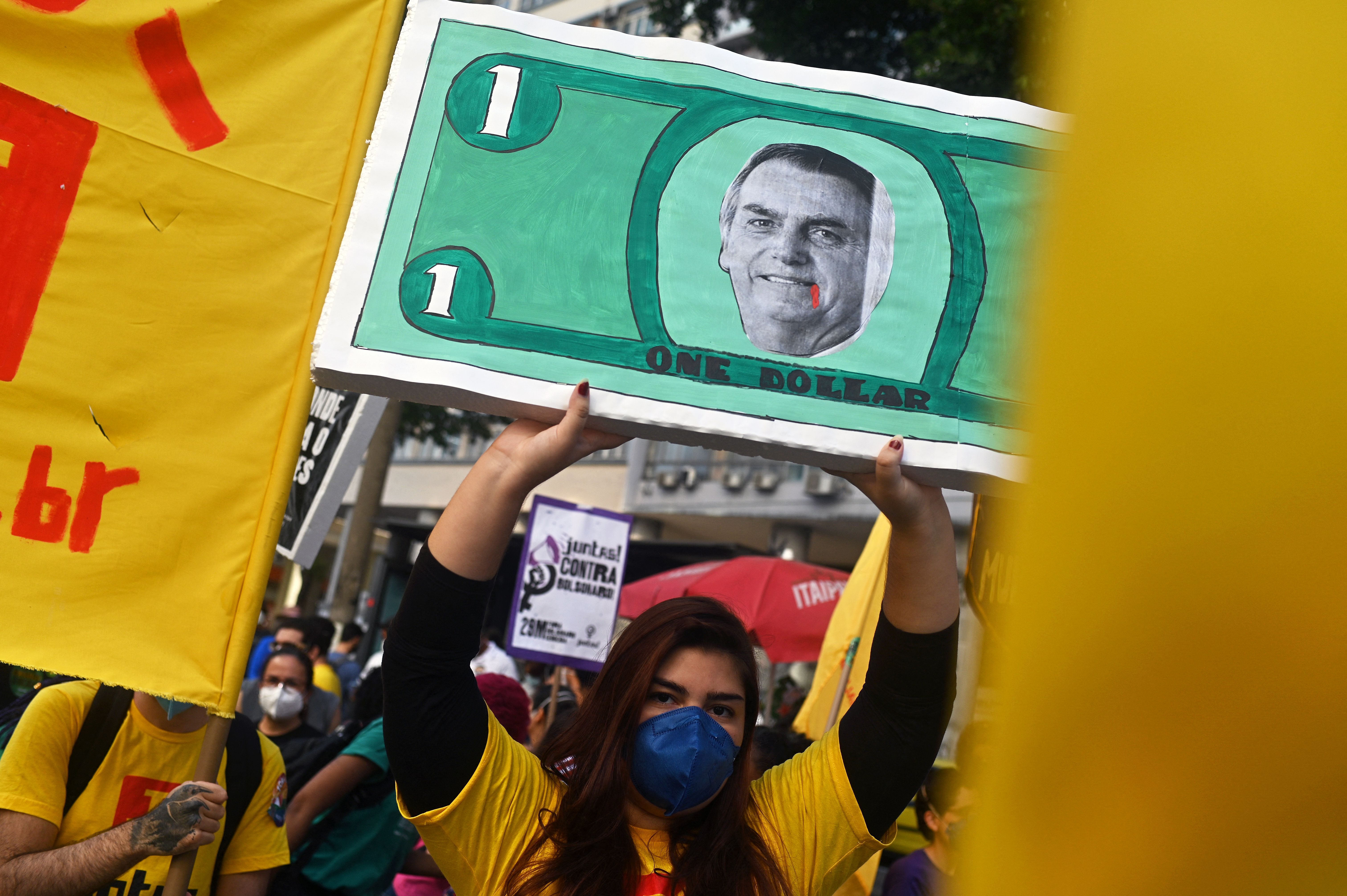  A woman holds a sign depicting Brazilian President Jair Bolsonaro in a dollar bill during a protest against his handling of the COVID-19 pandemic in downtown Rio de Janeiro, Brazil 