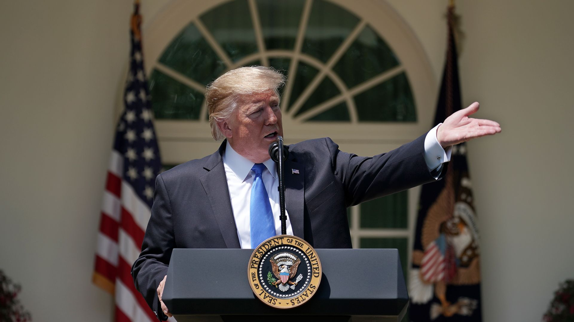 In this image, Trump gestures to the right while standing behind a podium.
