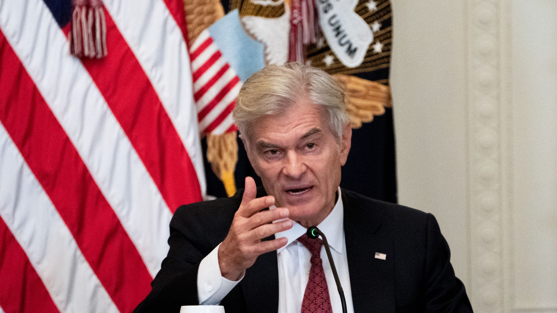 Mehmet Oz speaks on a podium in front of an American flag.