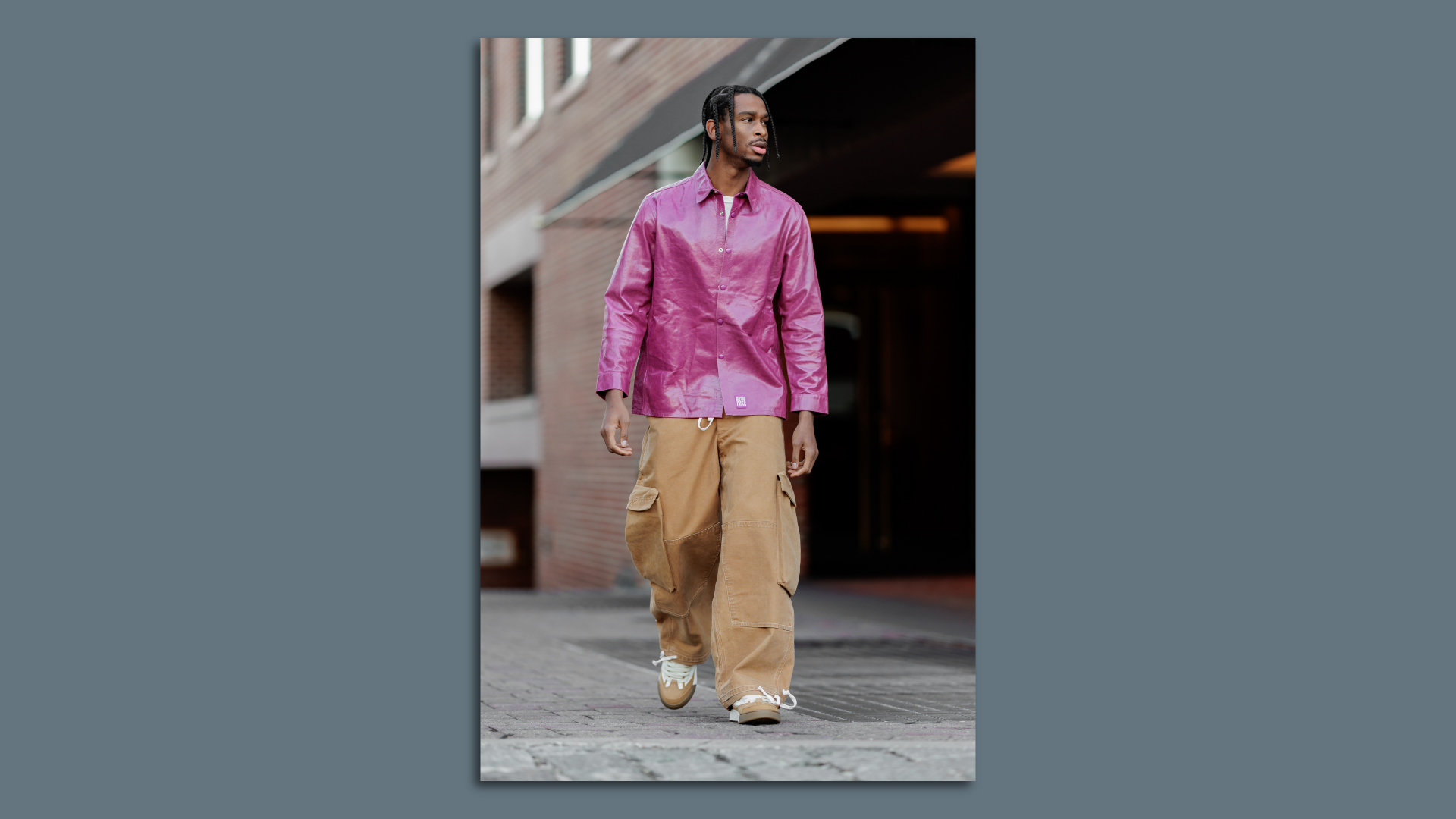 A man in a pink shirt and cargo pants walks the sidewalk