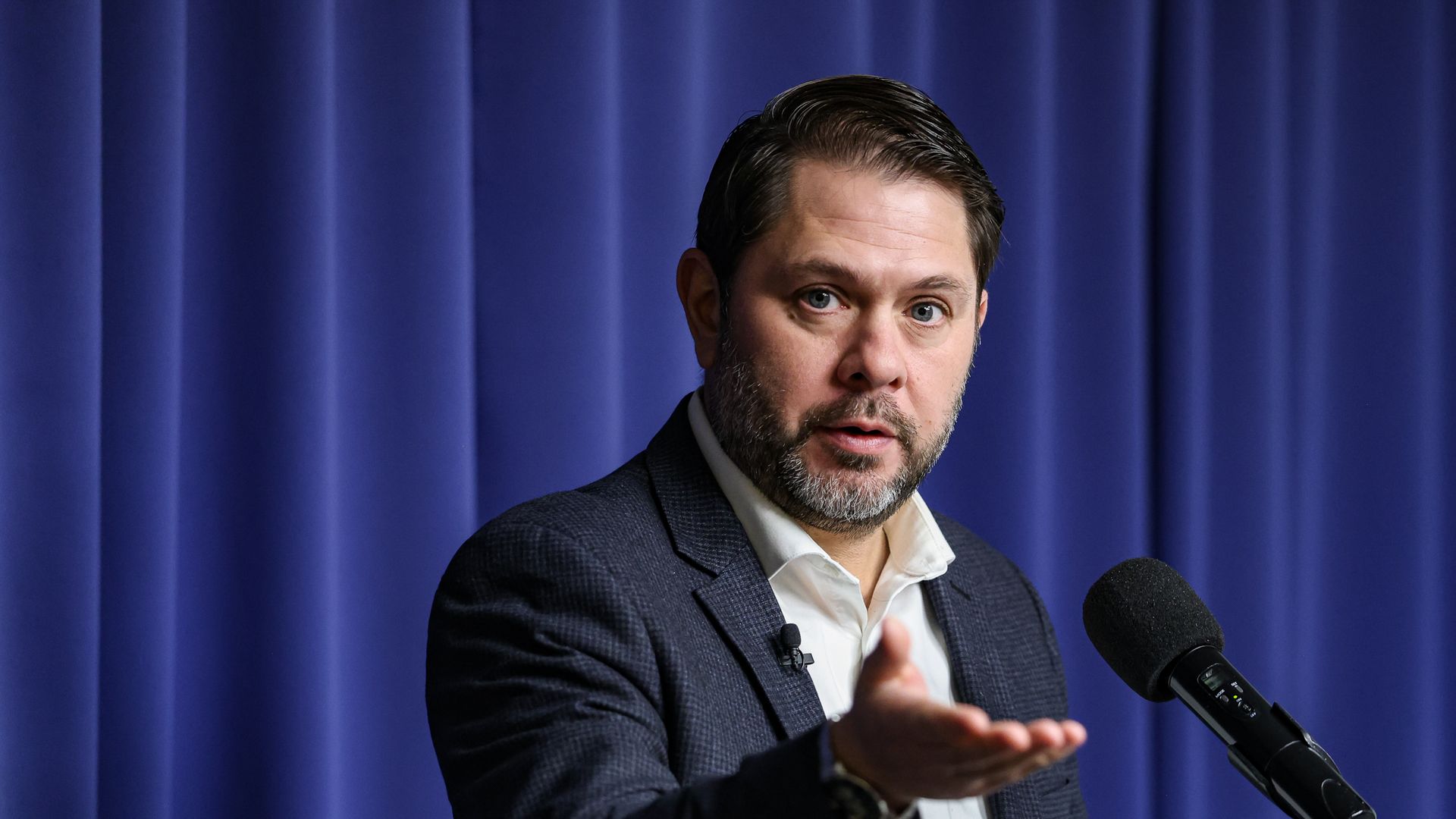 Arizona Sen. Ruben Gallego extends his hand while speaking into a microphone.