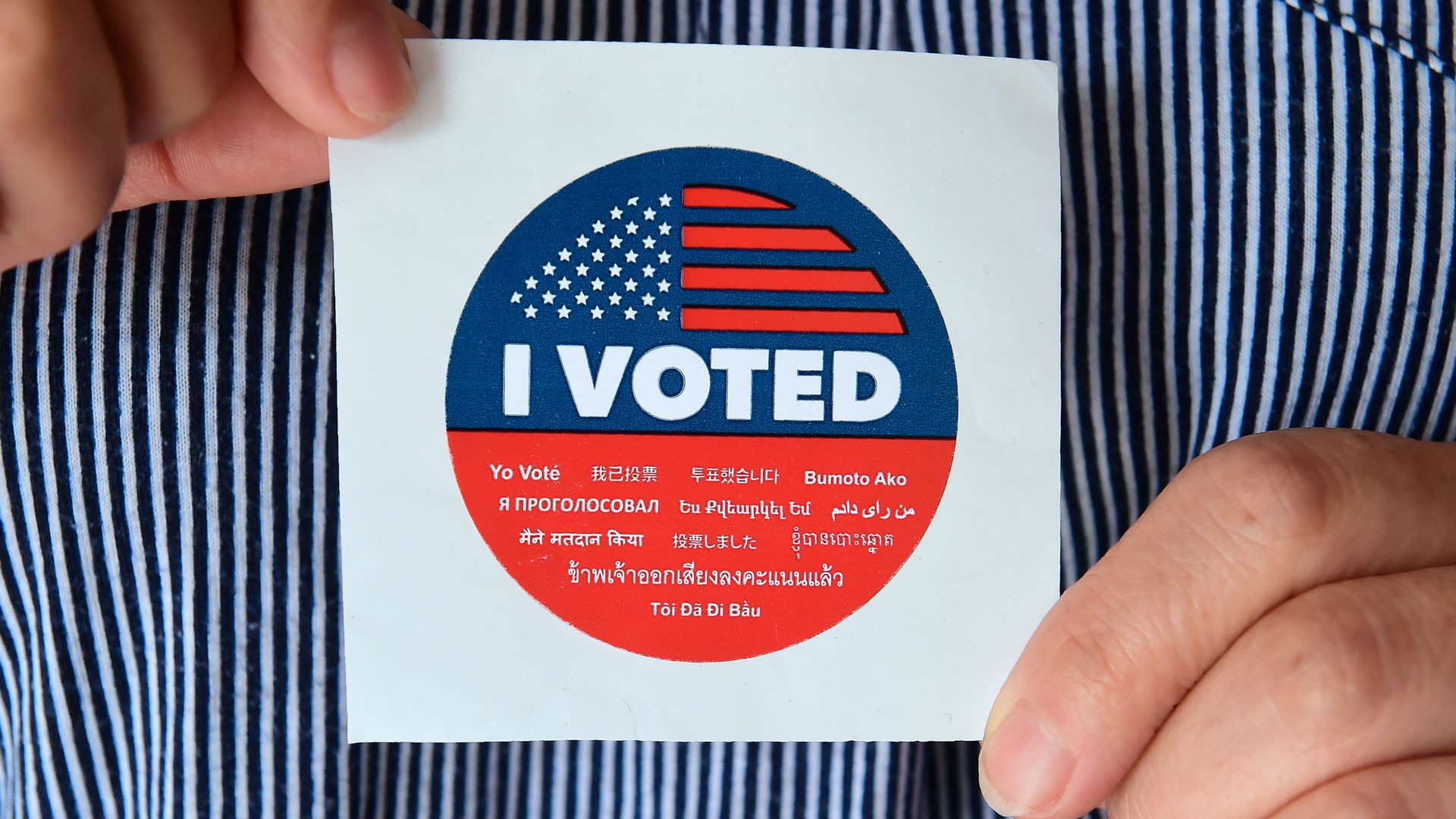 Fingers hold an "I voted" sticker.