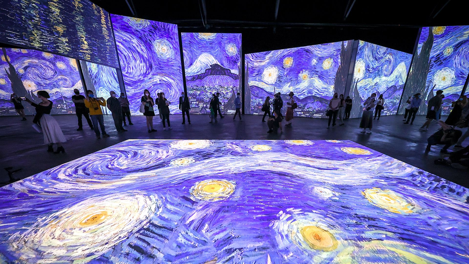 People walking around an immersive Van Gogh exhibit with "Starry Night" projected on screens around the room and the floor