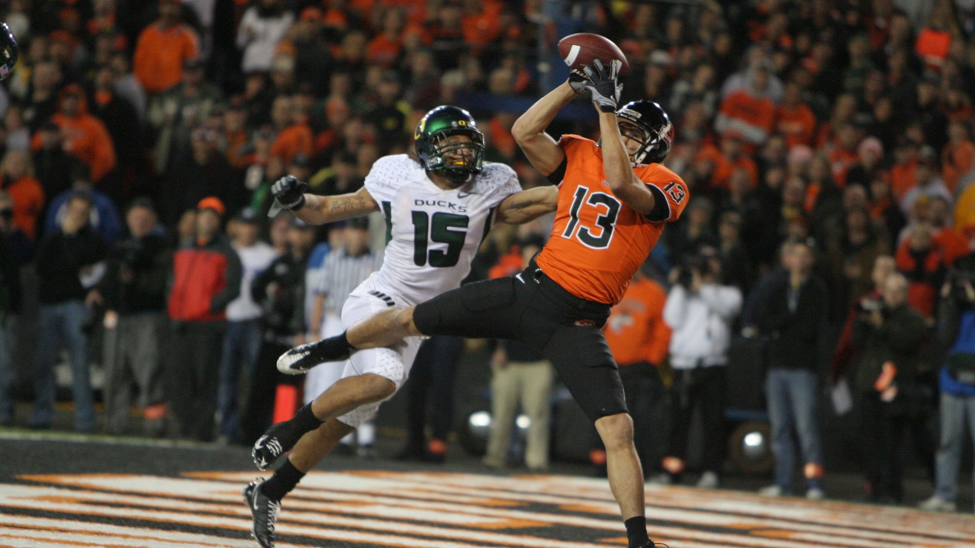 An Oregon state player catches a football during a game while an Oregon Unviersity player tries to tackle them