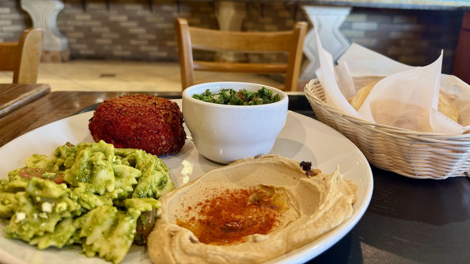 Plate of pita brea with pesto pasta; blurred restaurant counter and a person in the background.