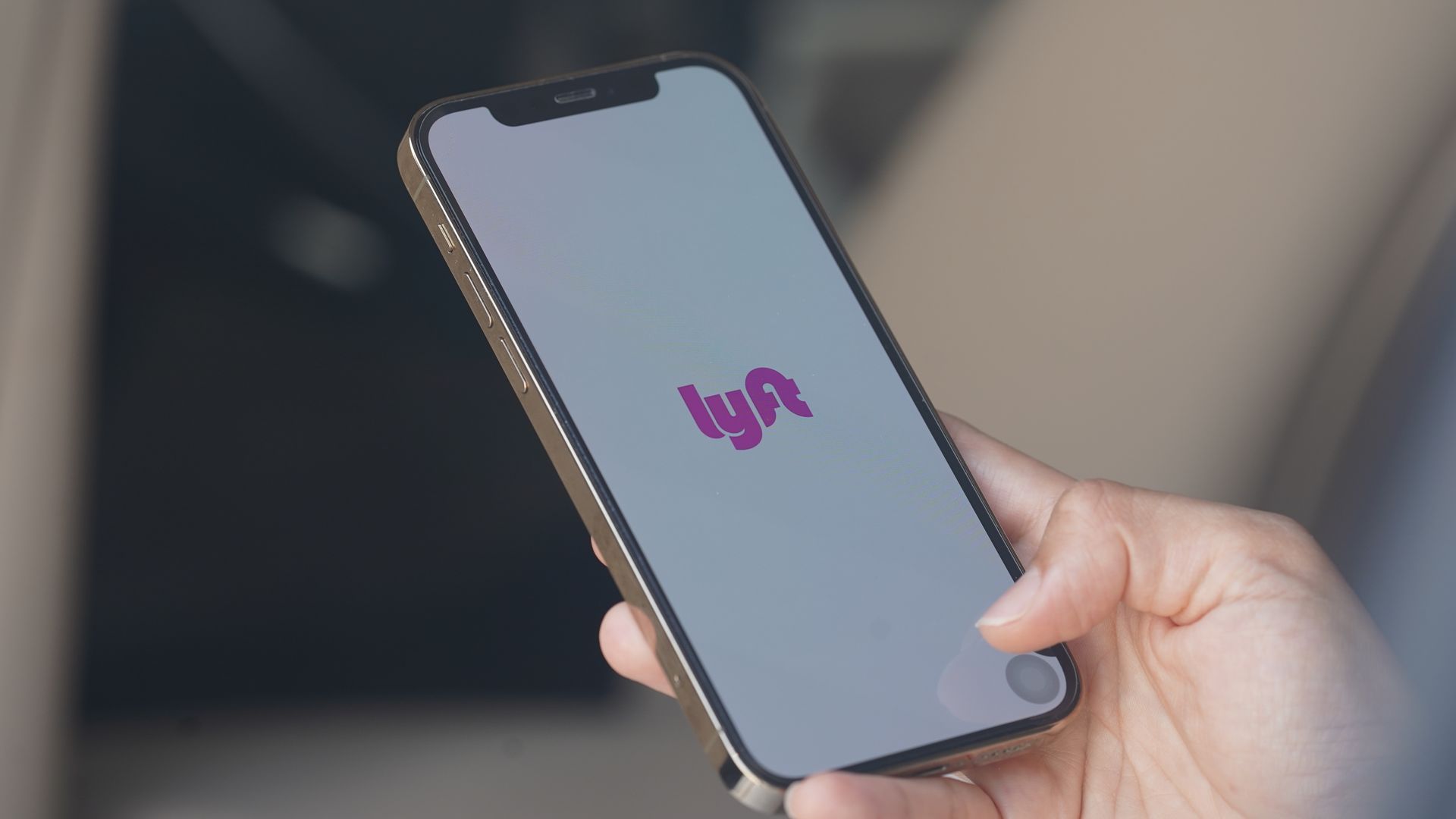 A hand holds a smartphone with the logo for the ride-hailing app Lyft on the screen.