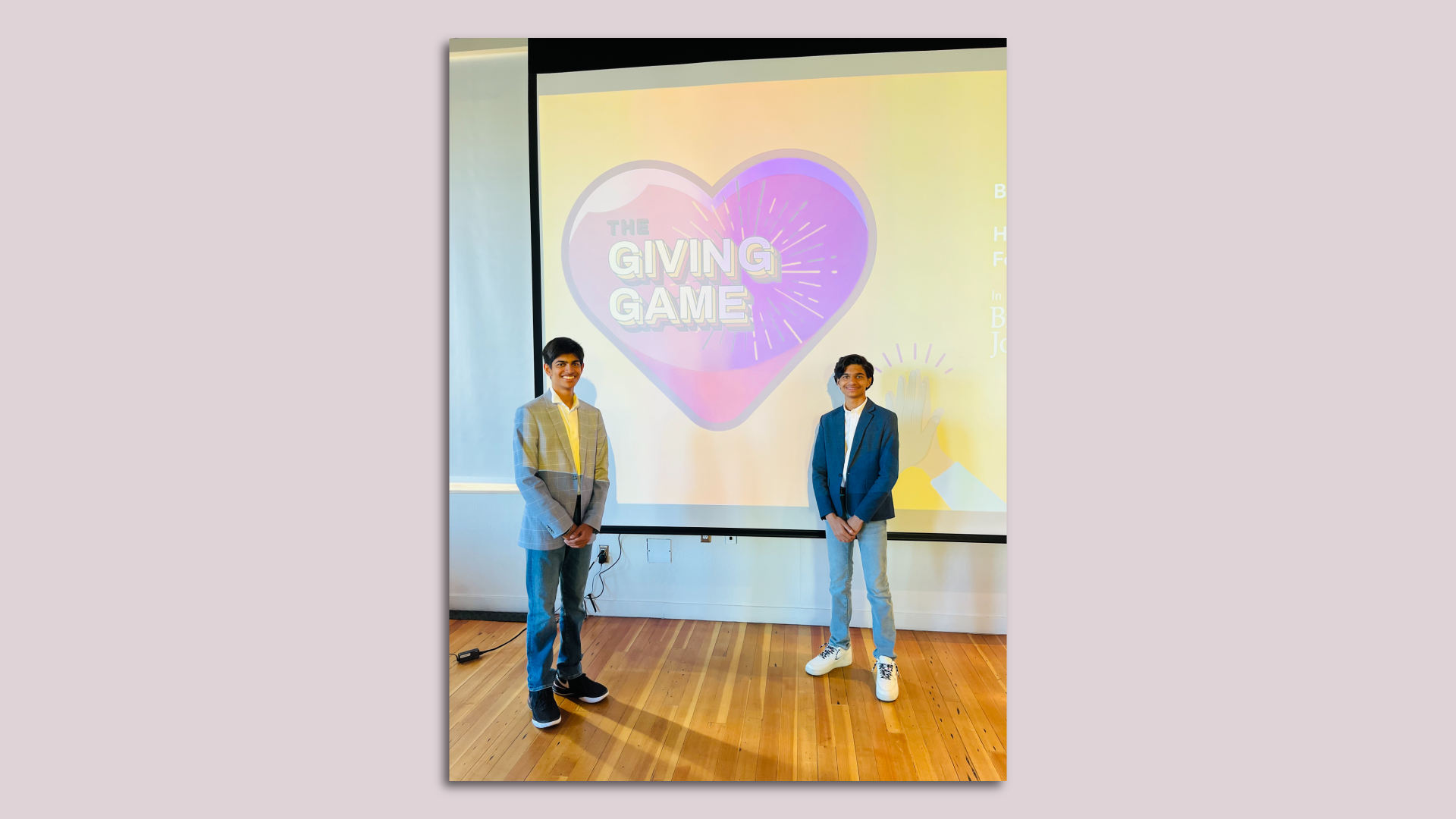 Two teenagers standing in front of a screen that says, "The Giving Game."