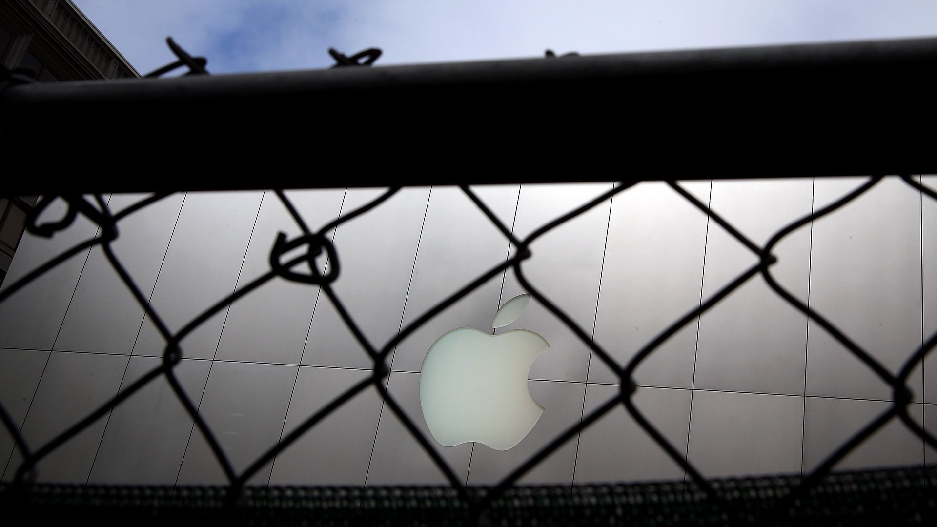 Apple laptop with its log as seen outside through a chain link fence
