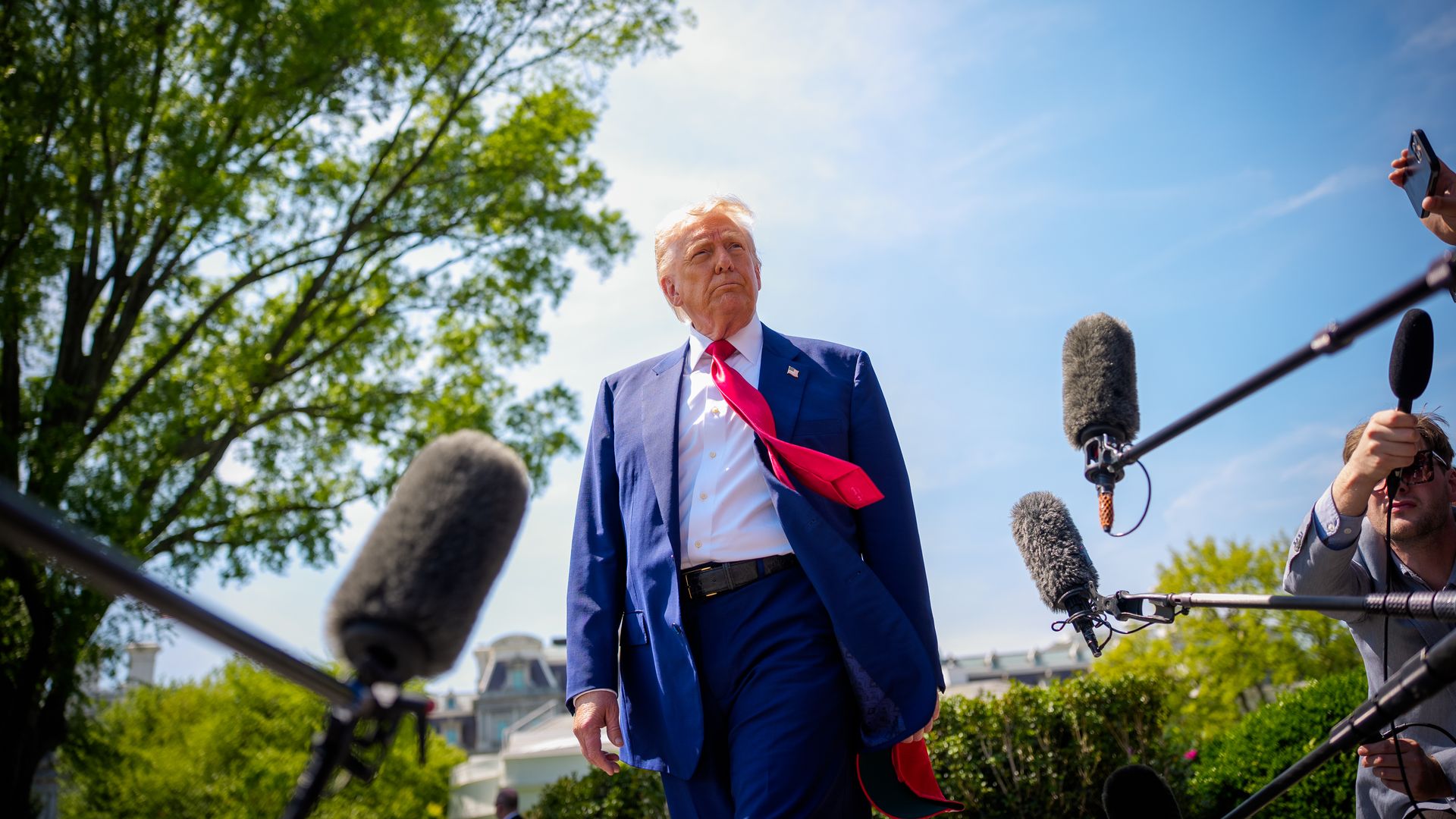 Trump walks by reporters' microphones as his tie blows in the wind.