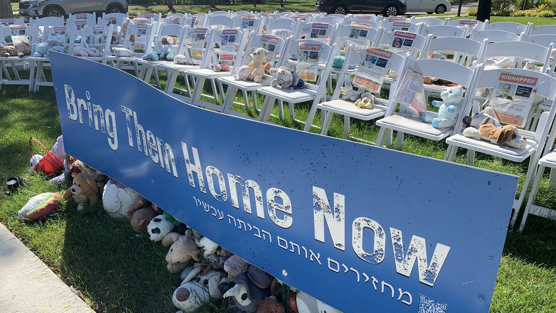 Photo of a sign that says "Bring Them Home Now" with empty chairs behind it 