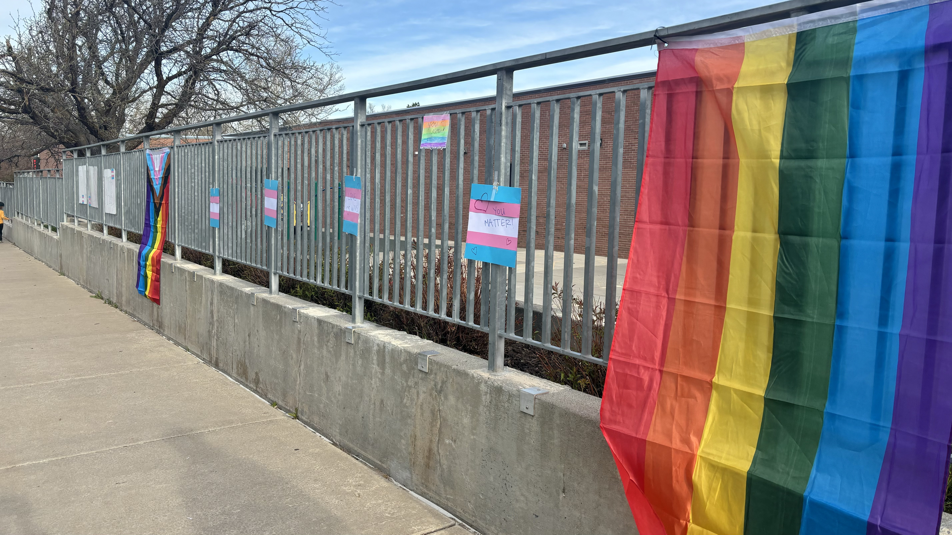 Transgender and Pride flags are placed on a gate.