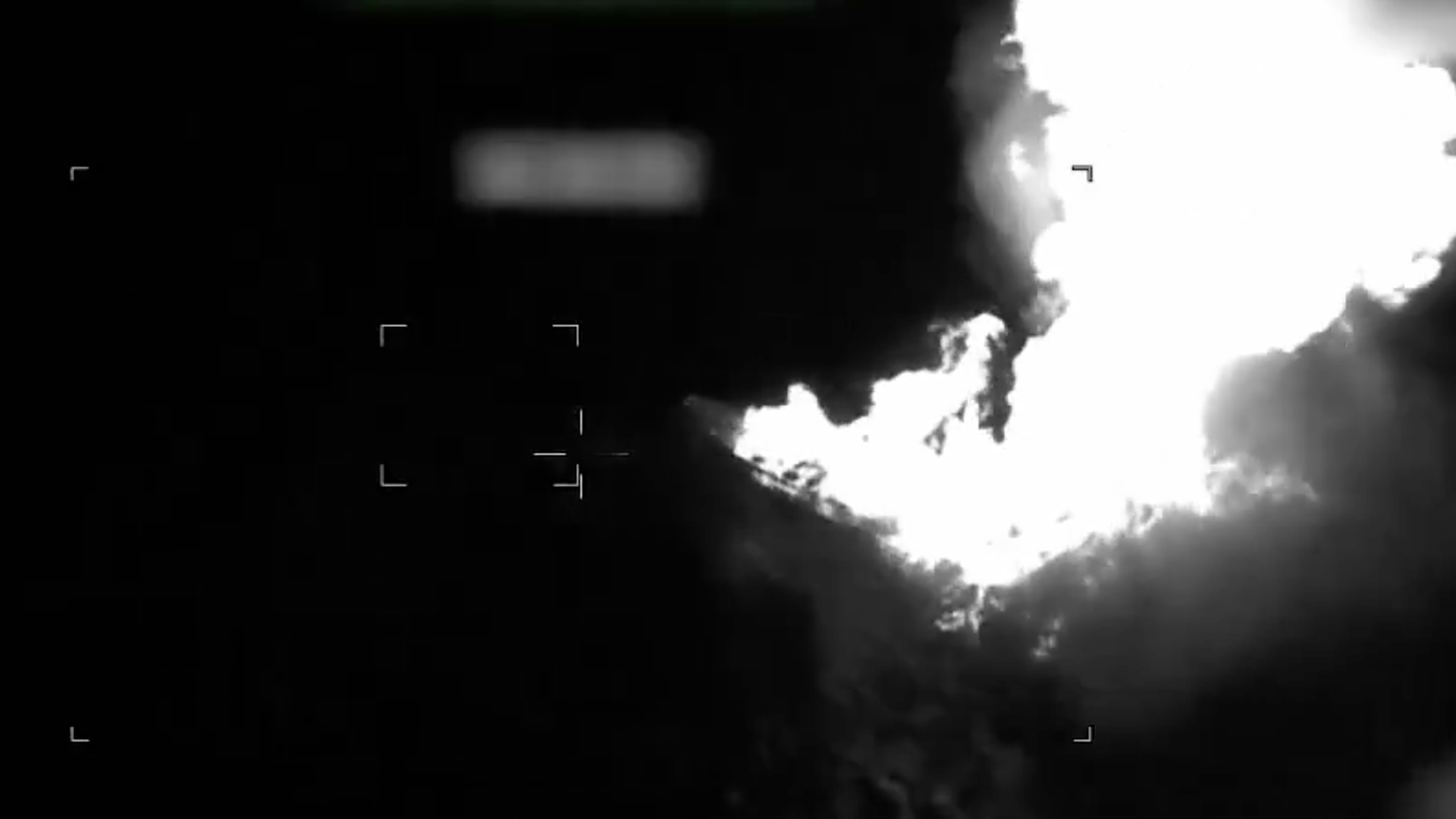 Black-and-white night-vision frame showing a bright fireball/explosion on the right.