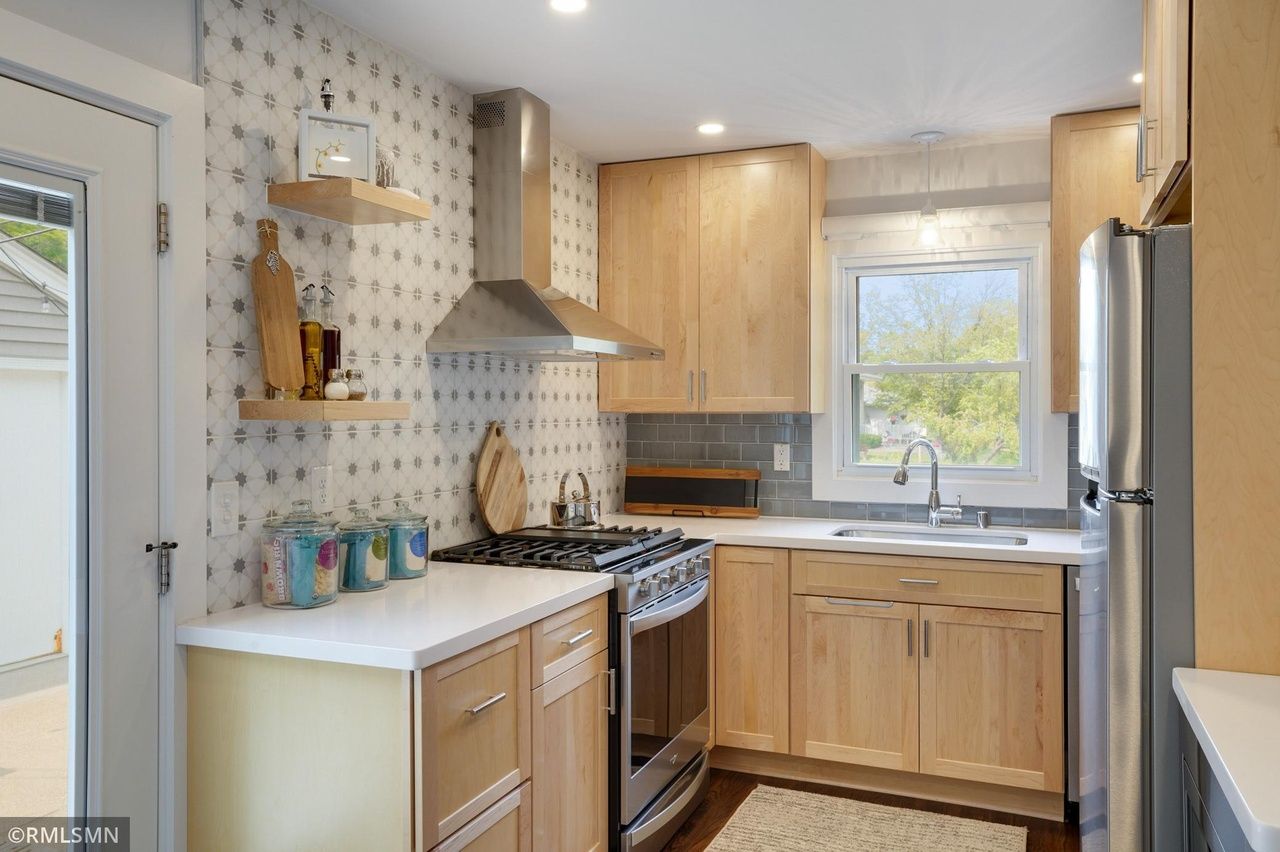 modern kitchen with light wood cabinetry, patterned backsplash and floating shelves