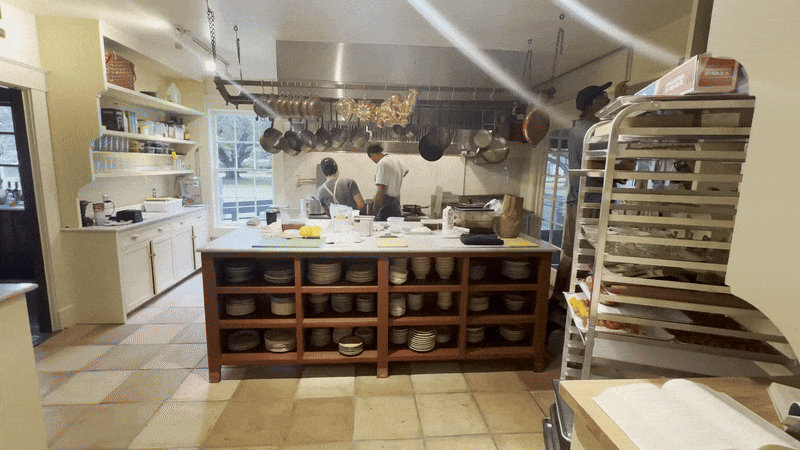 Two chefs work at a stove across a kitchen.