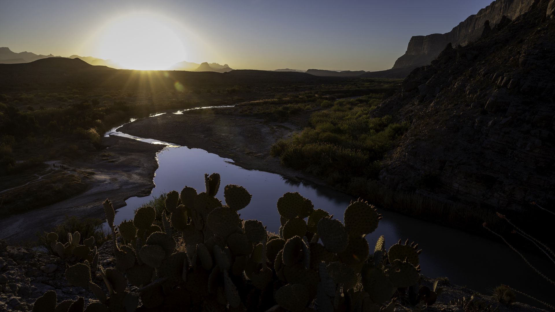 An image of the sun rising over the Rio Grande in Big Bend National Park, with a prickly pear cactus in front.