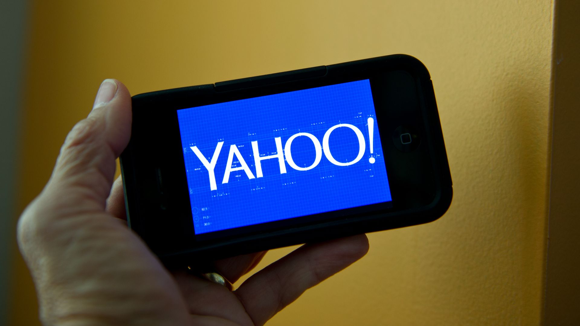 A hand holds a phone with the Yahoo logo.
