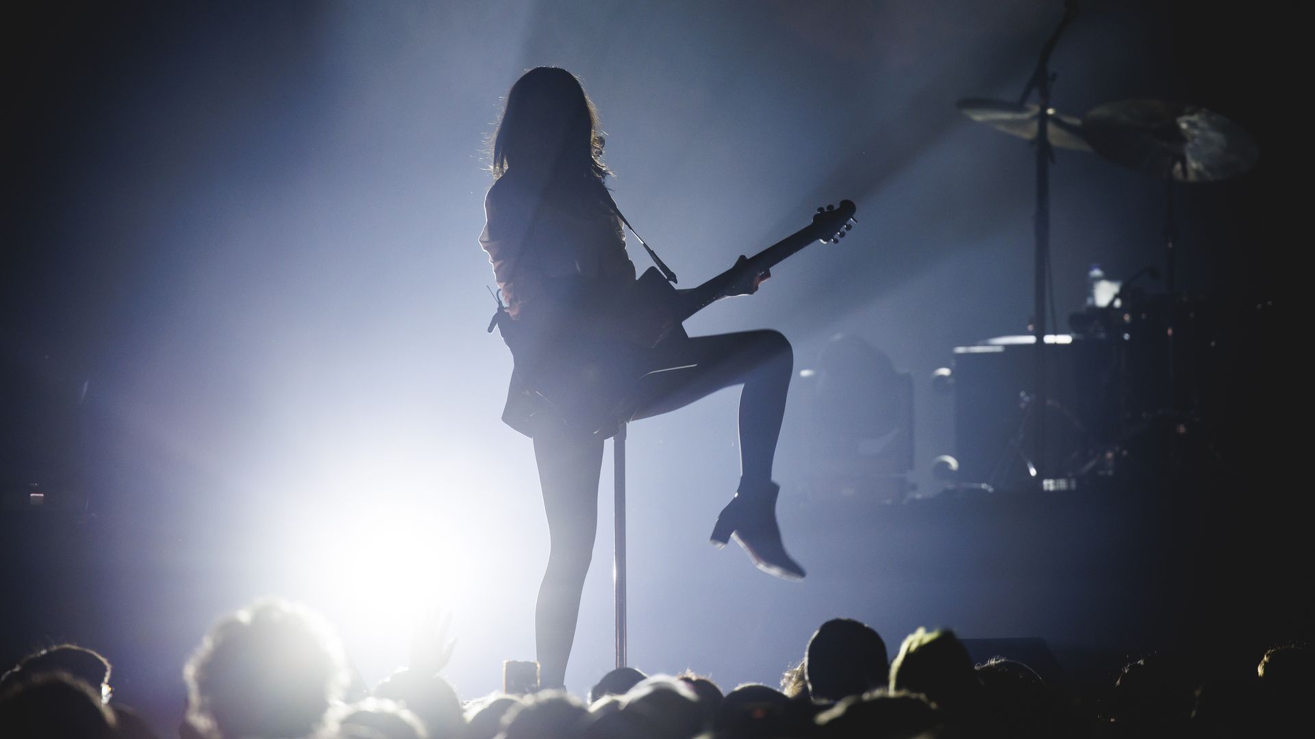 A silhouette of St. Vincent performing with a stage light illuminating her from behind