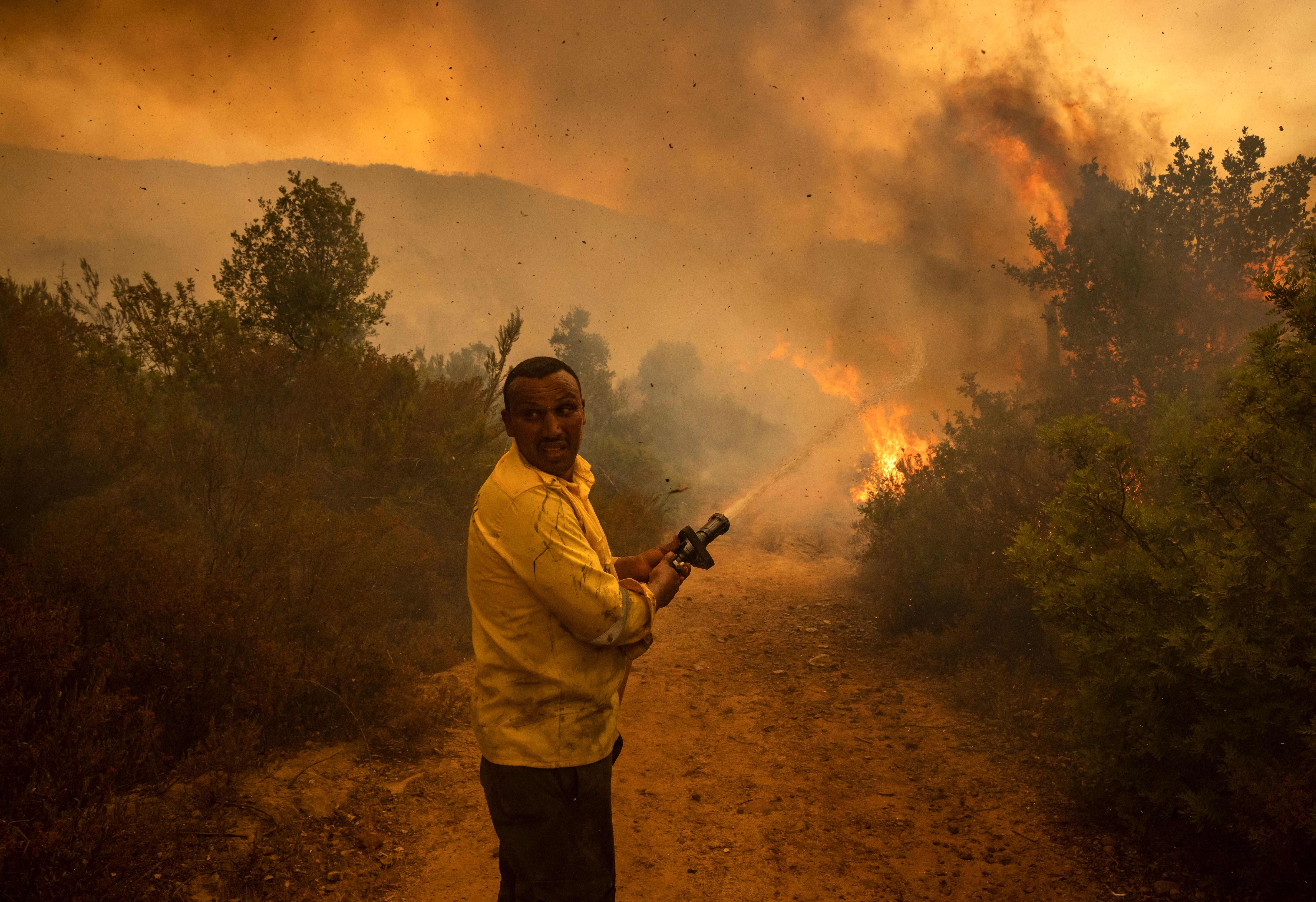 A forest ranger sprays water from a hose on a forest fire near the Moroccan city of Ksar el-Kebir in the Larache region, on July 15.