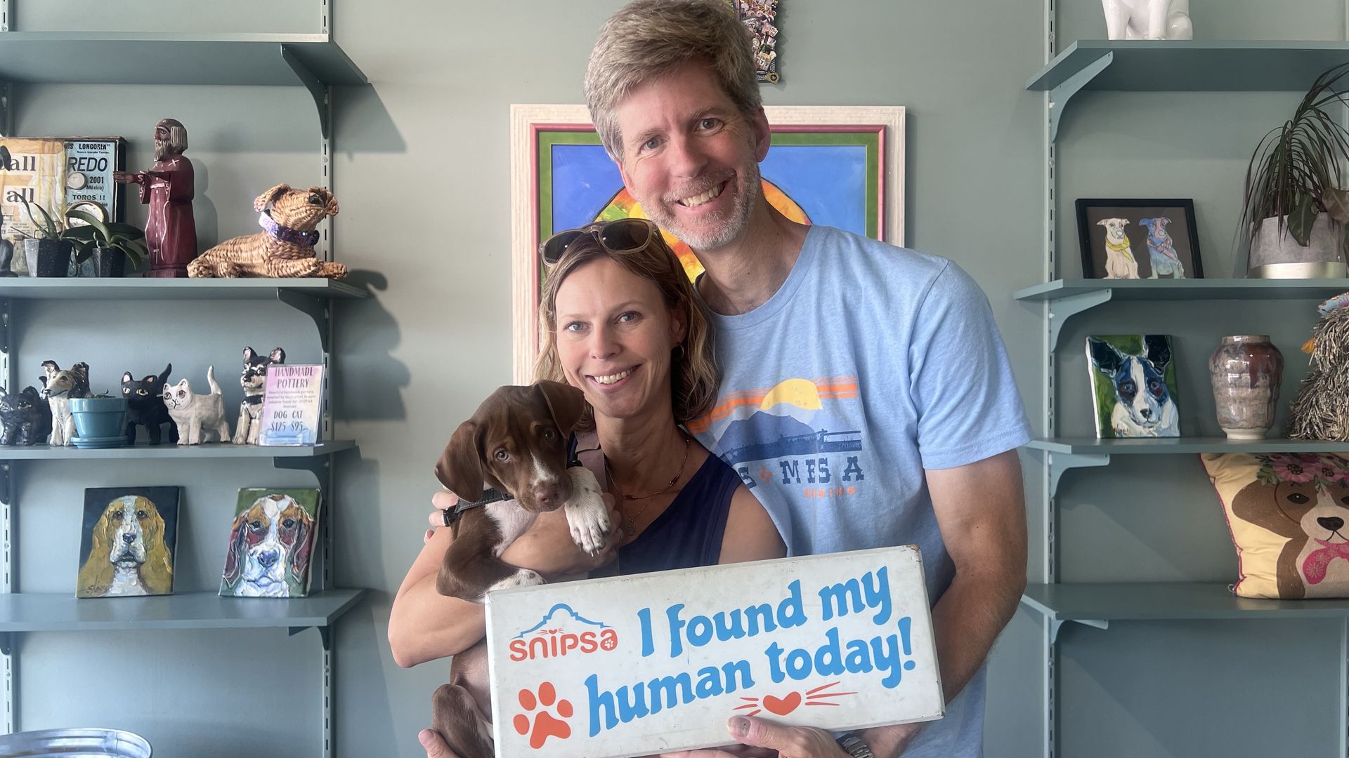 A man and woman smile while holding a brown puppy.