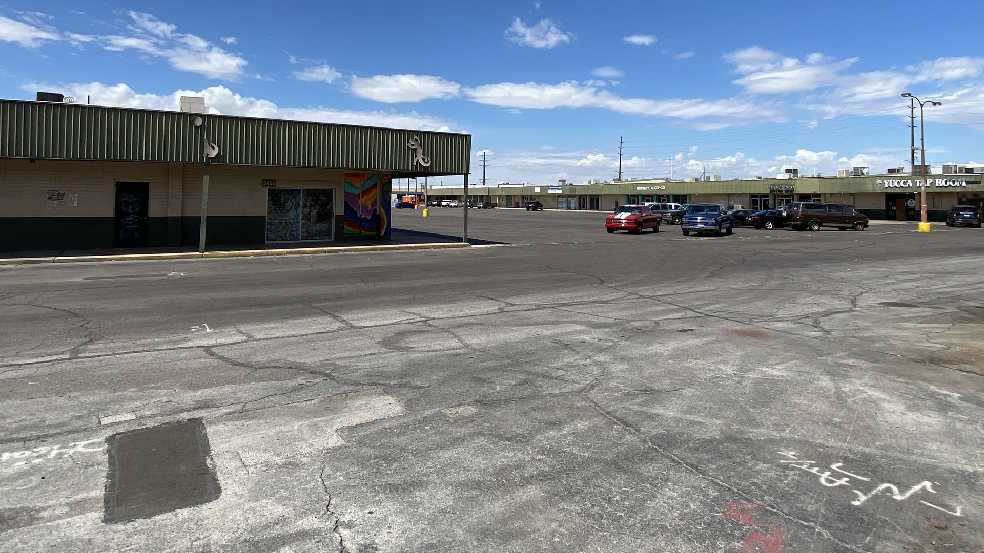 A run down commercial plaza with a parking lot running between two one story buildings.