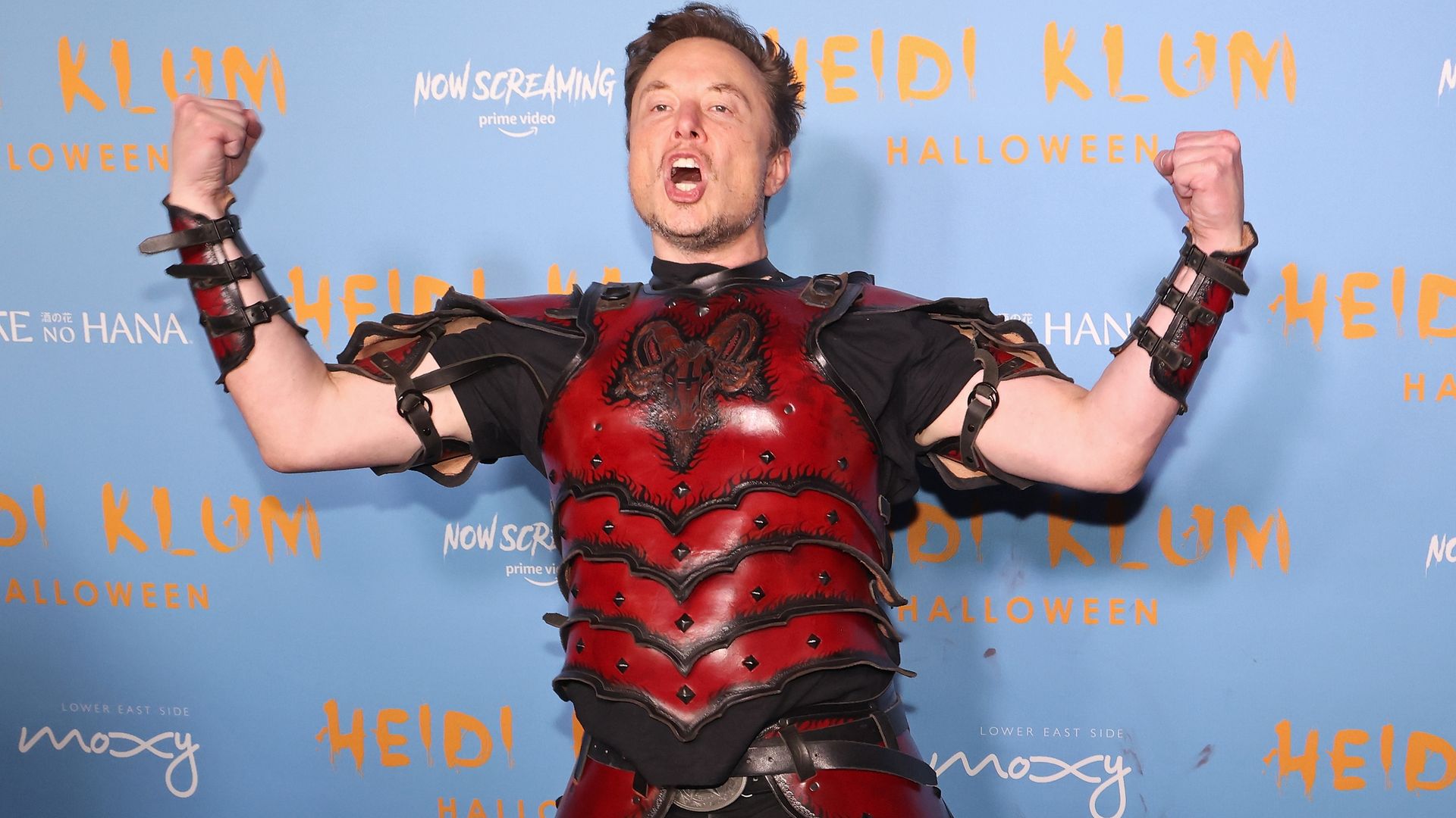 Photo of Elon Musk with fists and arms raised wearing superhero Hollywood costume 