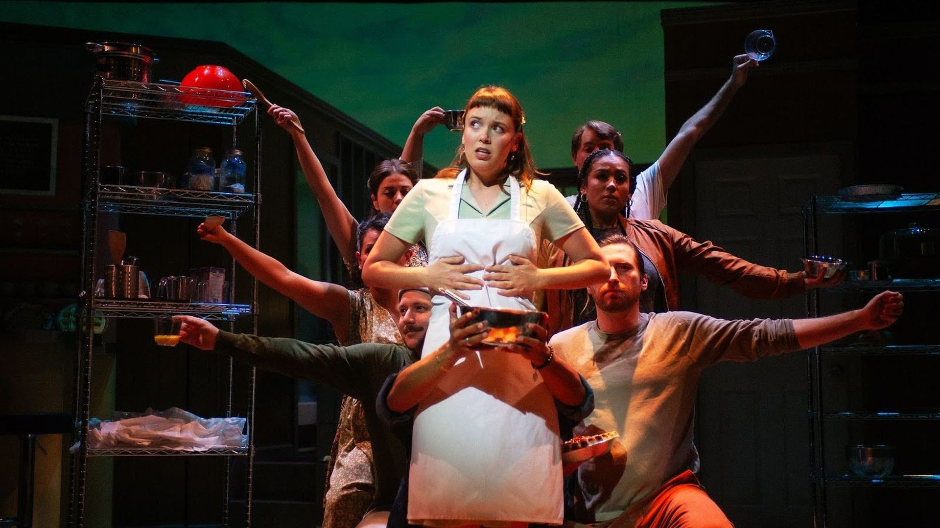 Photo of a woman on stage with other cast members holding pots and pans behind her