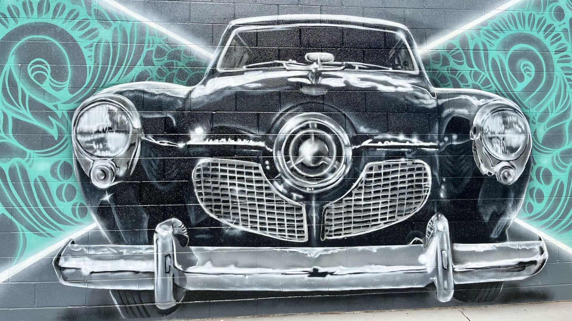 A mural of black-and-white car against a turquoise pattern background.