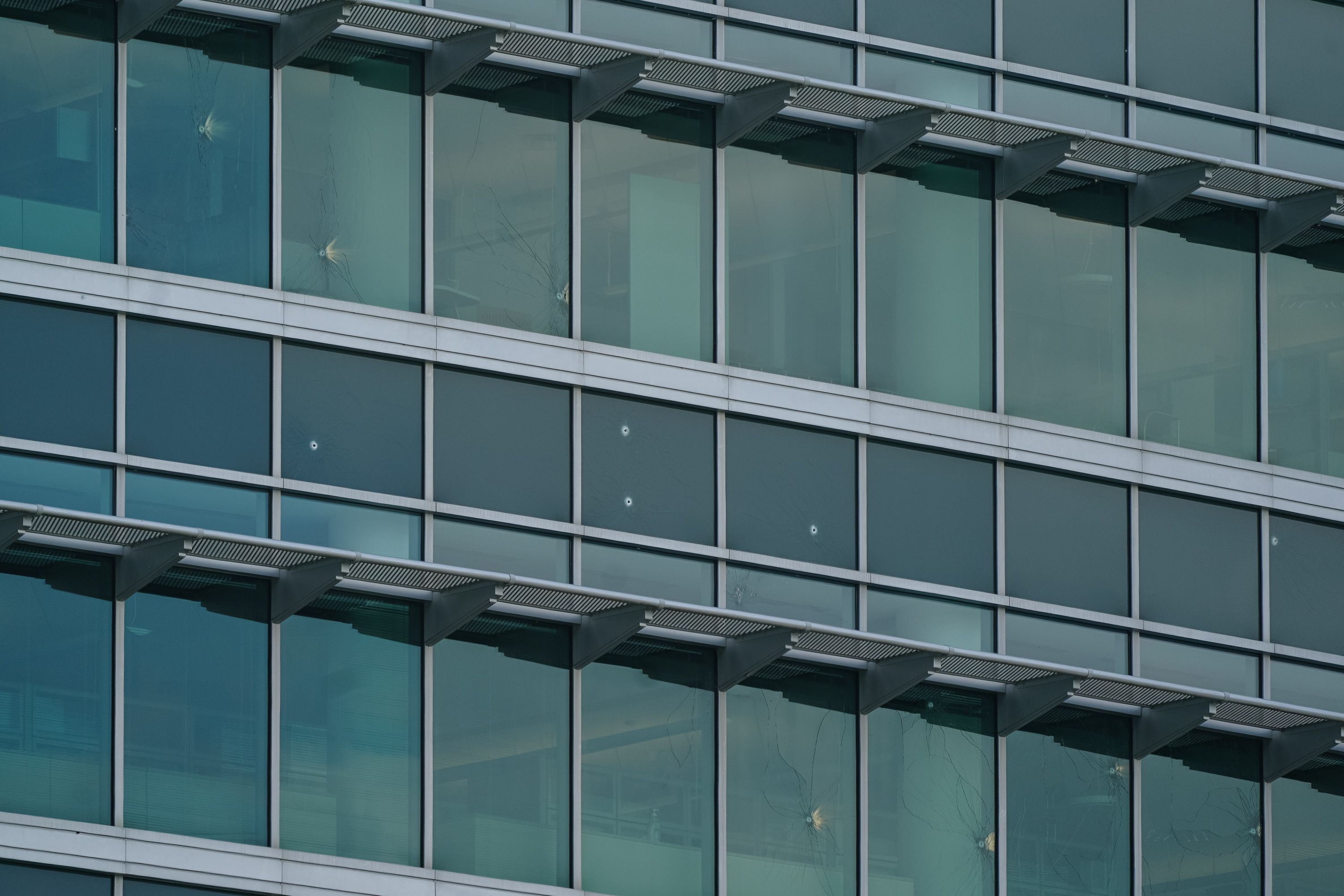 Close-up of a modern glass building facade with several bullet holes causing cracks in the window panes.