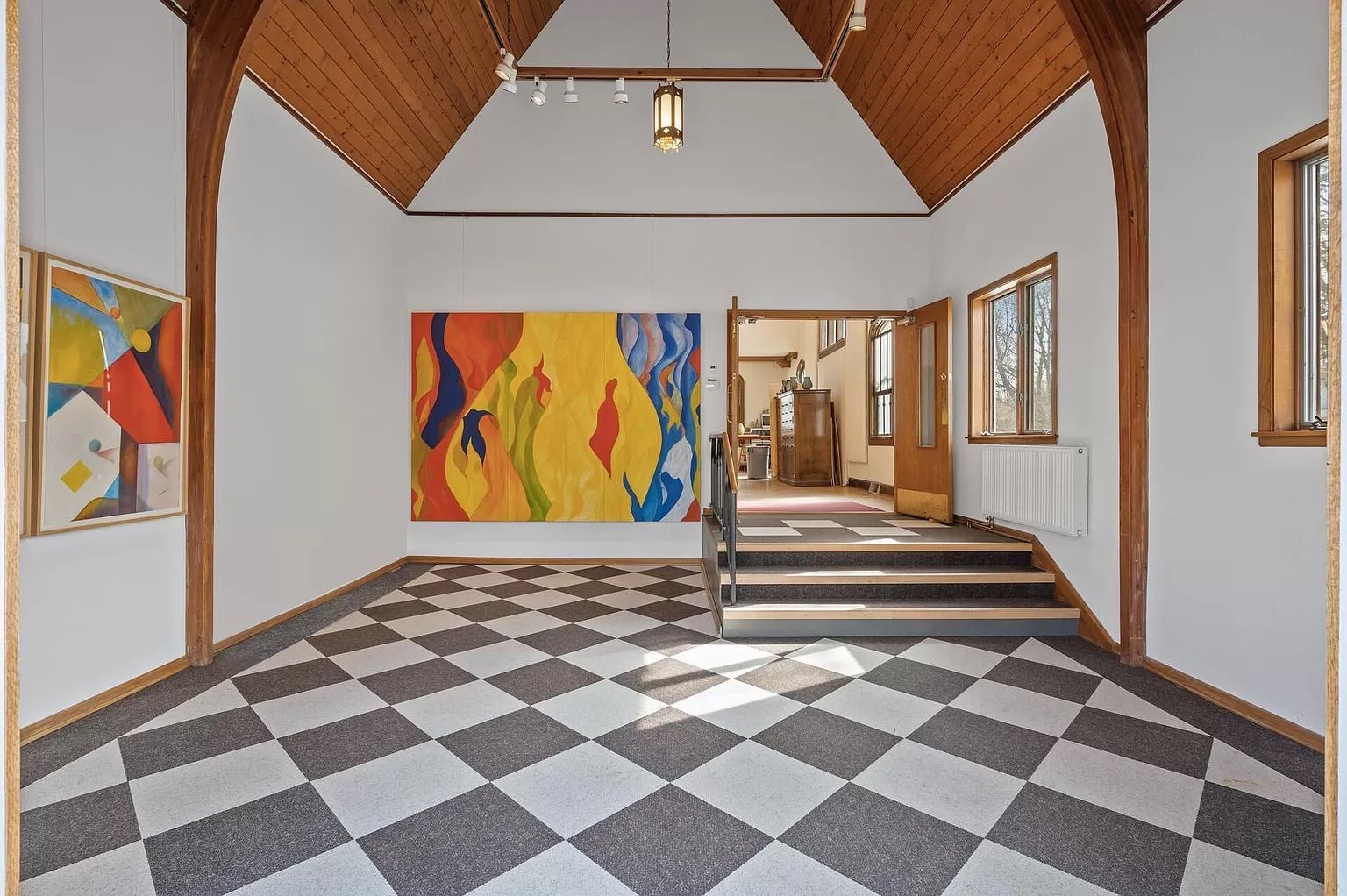 A room with checkered black and white floors and colorful paintings on the walls.