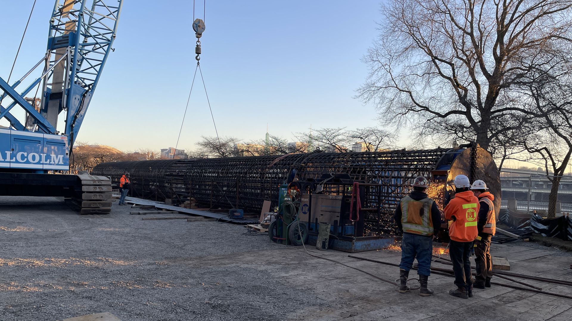 Several construction workers stand next to a crane and a large rebar cage.