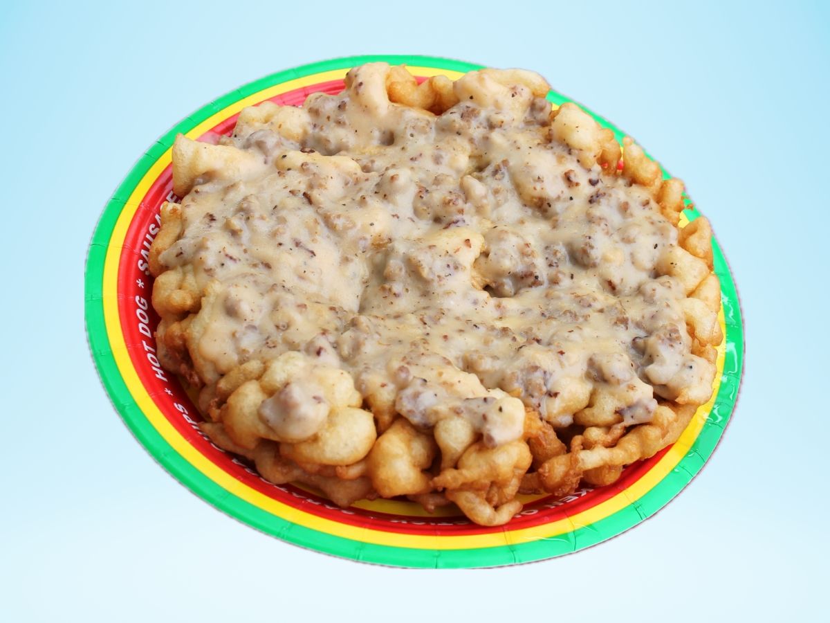 A paper plate with a green, yellow and red border with a funnel cake on it topped with a tannish-gray gravy.