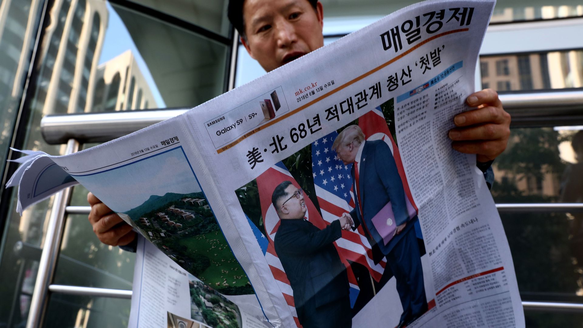 An Asian man reading a newspaper with a photo of Kim Jong-un and Donald Trump shaking hands on the front page