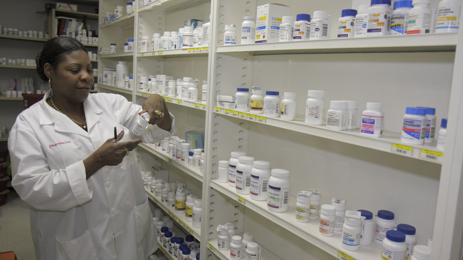 A pharmacist looks at medication bottles in a pharmacy.