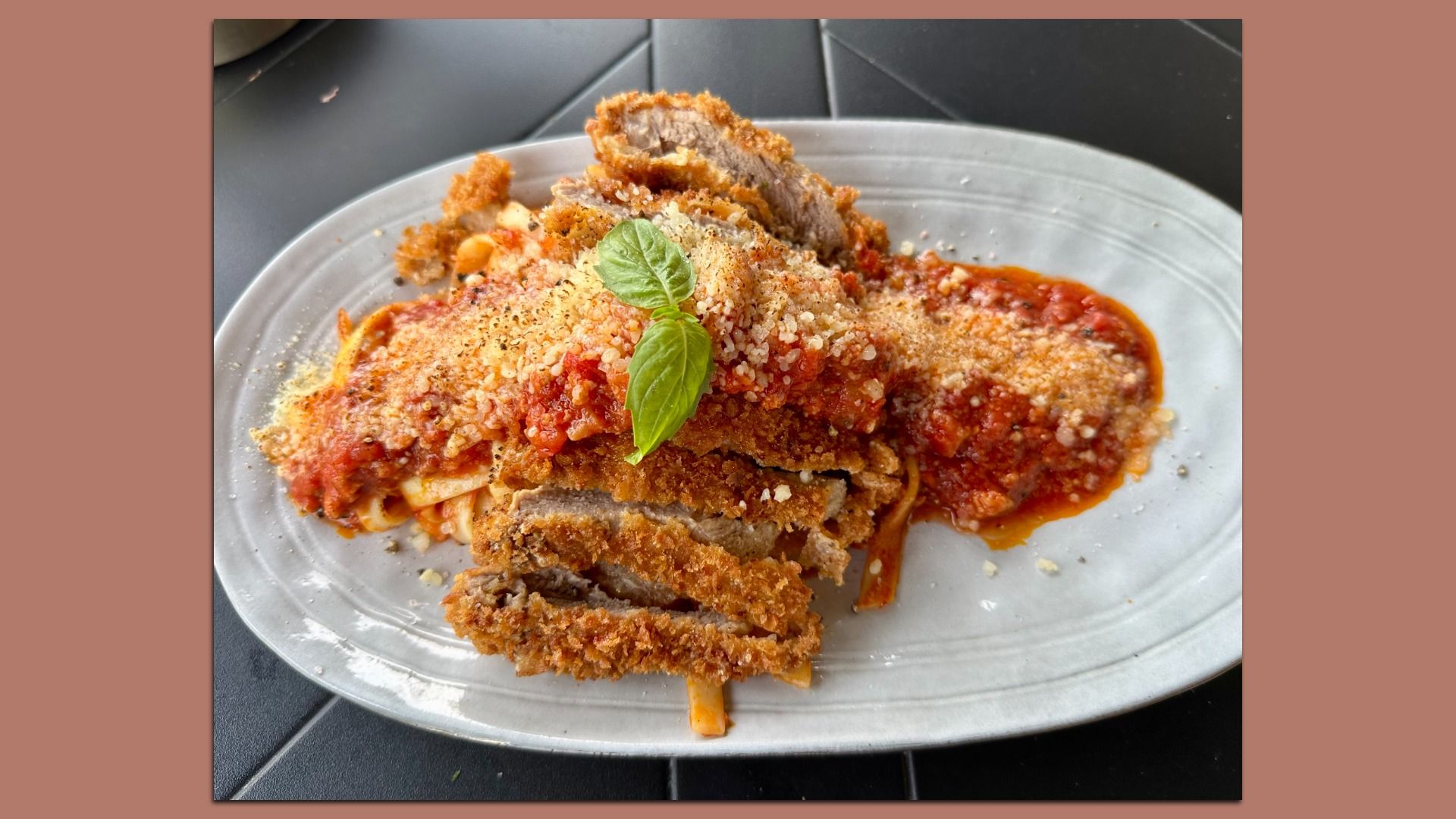 Plate of spaghetti with red tomato sauce and crispy breaded meat cutlets, topped with grated cheese and a fresh basil leaf on a gray plate.