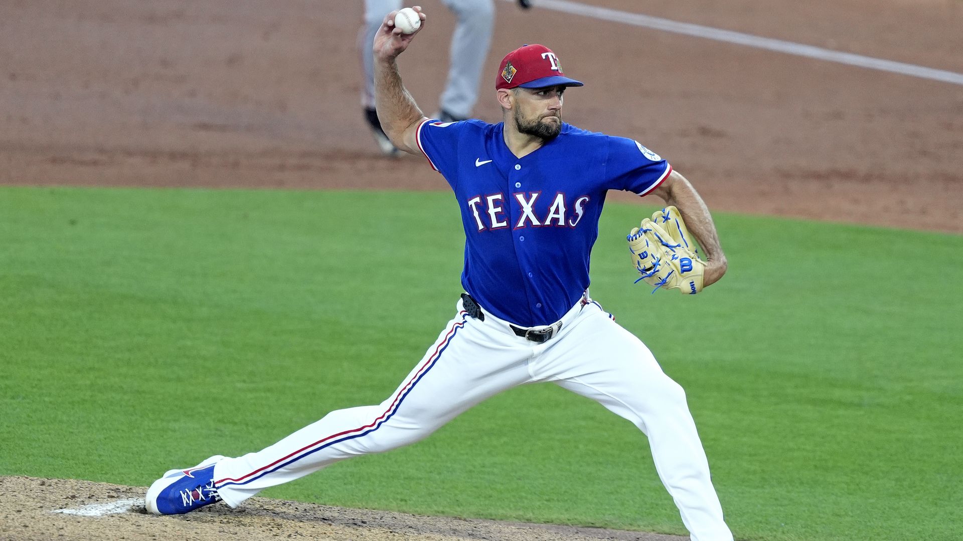 Texas Rangers pitcher Nathan Eovaldi wears a blue jersey while throwing a pitch with his right artm 