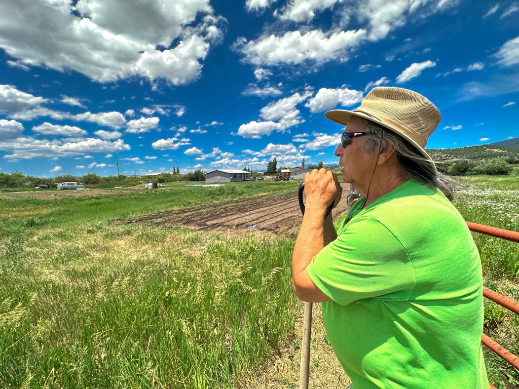 Manuel Trujillo looking over his farm in Ensenada, New Mexico while resting on a shovel. 