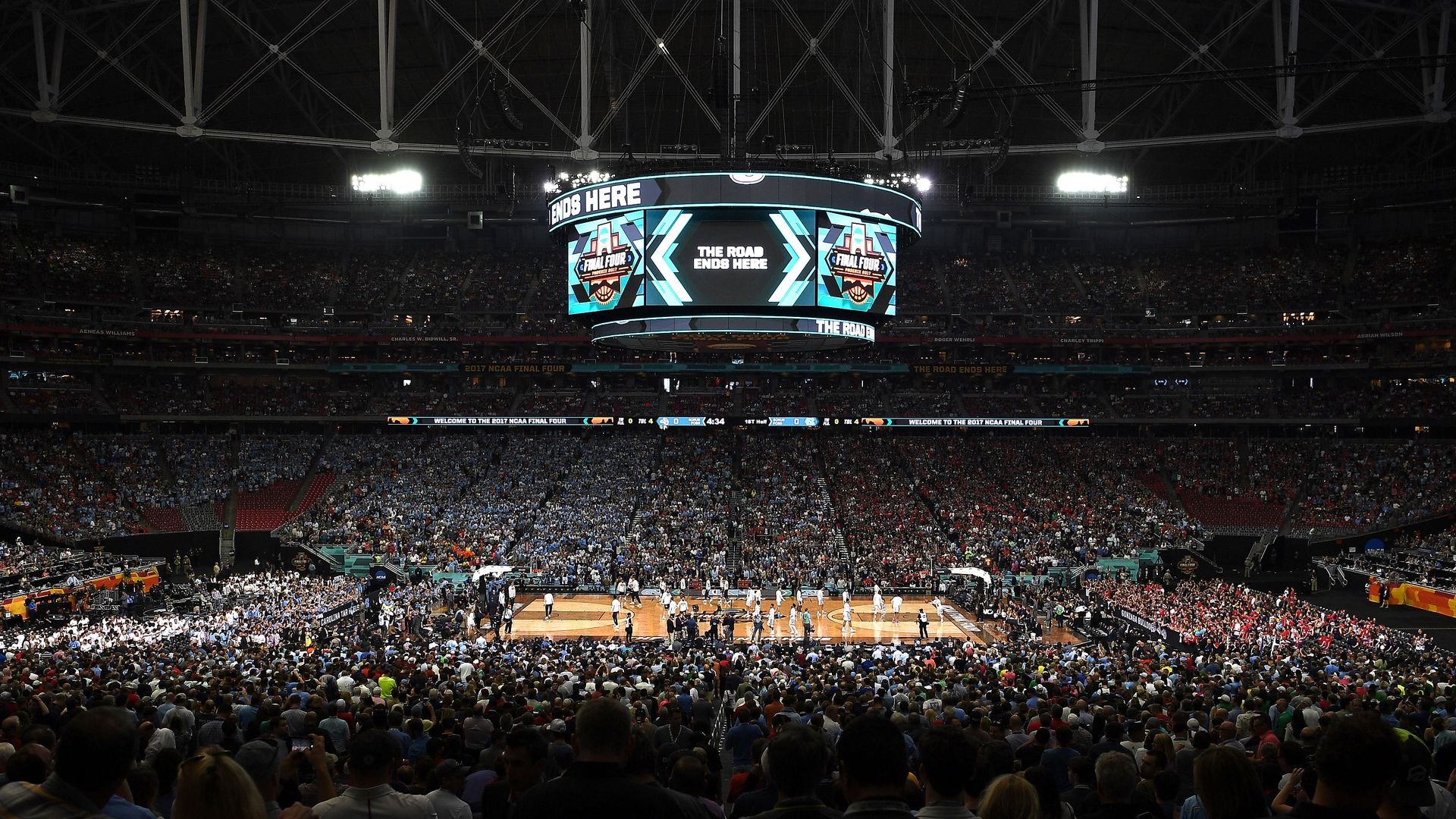 tens of thousands of people in a basketball stadium with a large scoreboard hanging in the middle.
