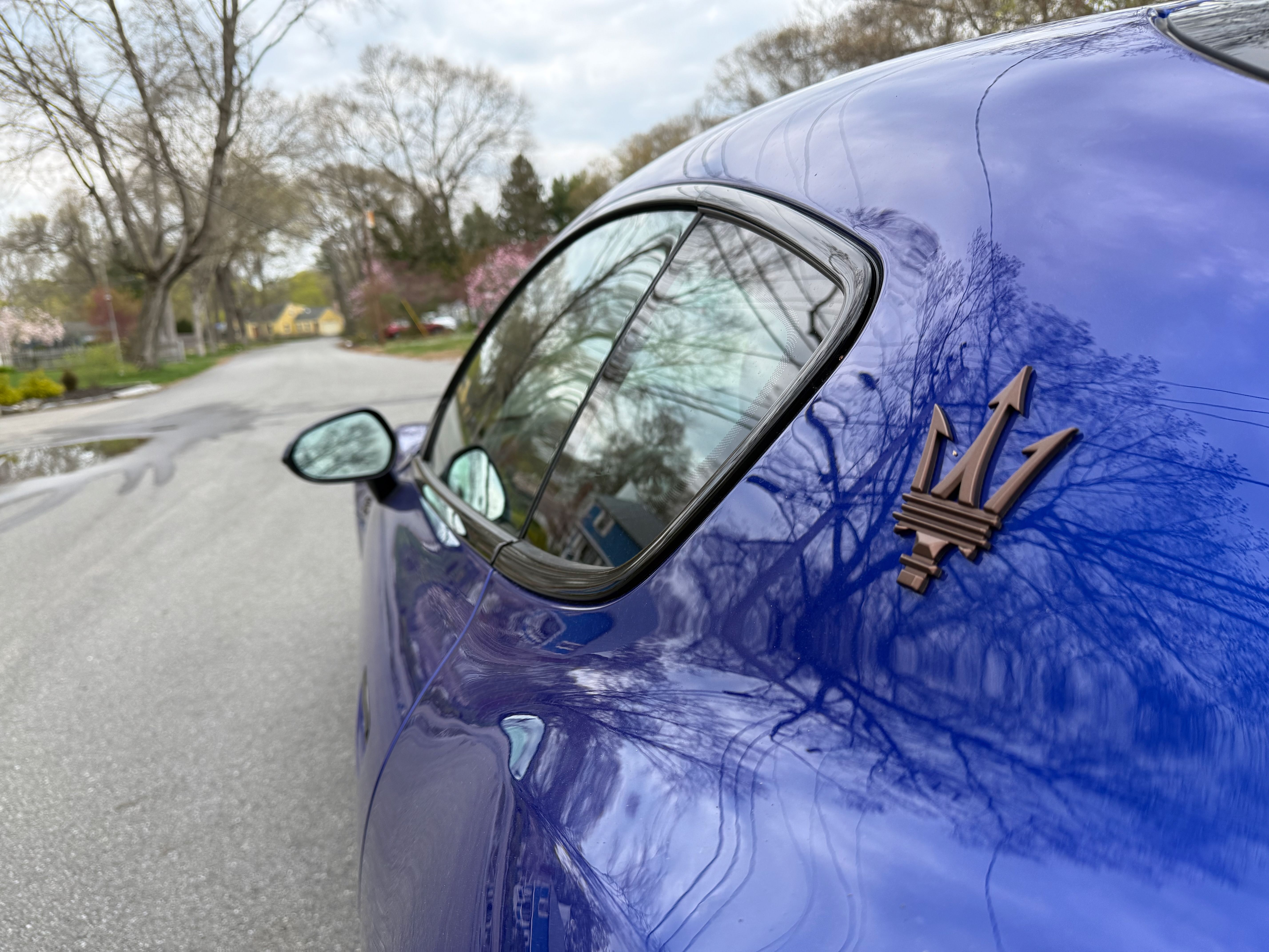 A close-up of the Maserati logo on the bright blue exterior of the Folgore GranTurismo.