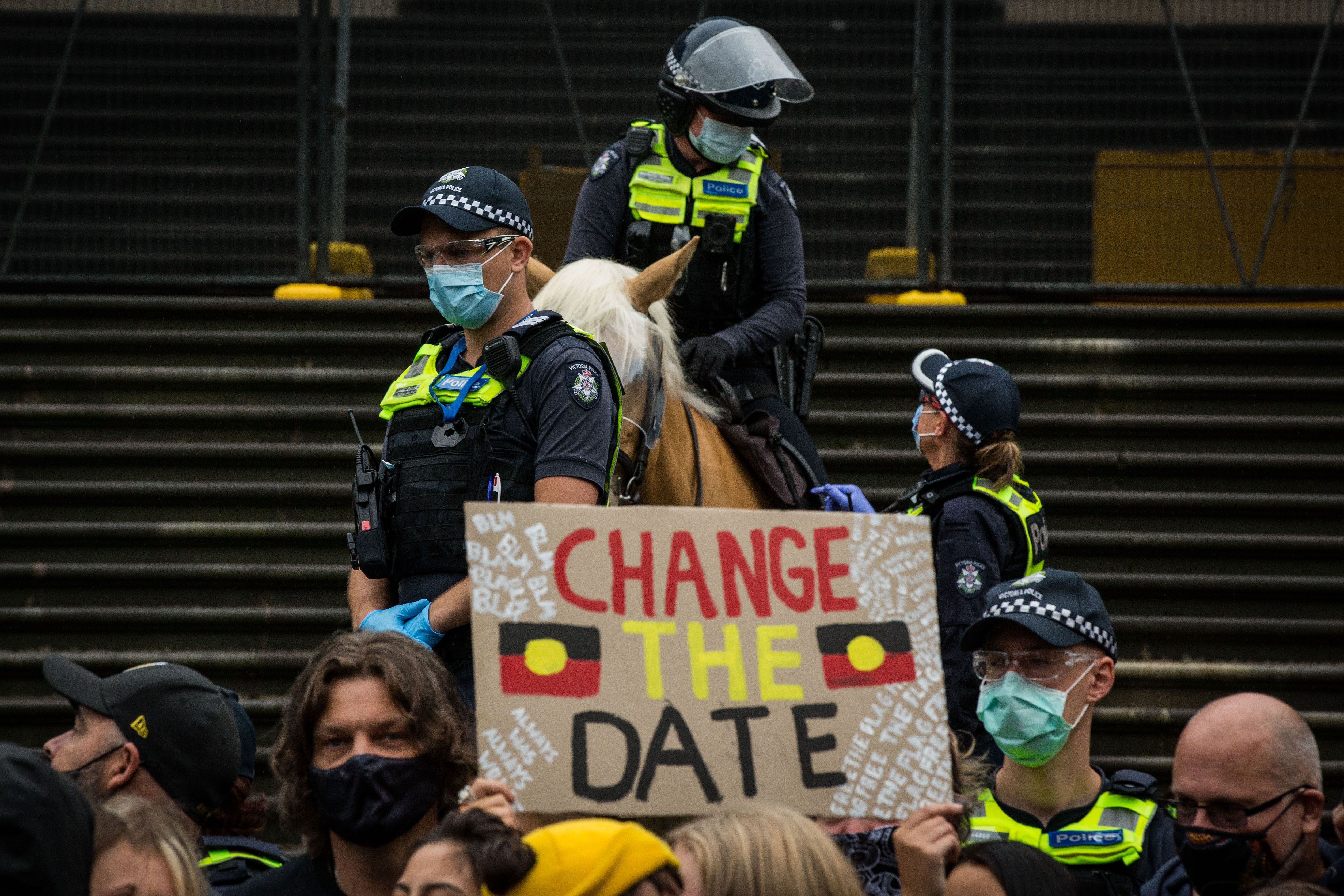 Police officers stand watch as protesters display signs at the Invasion Day rally in the city on January 26